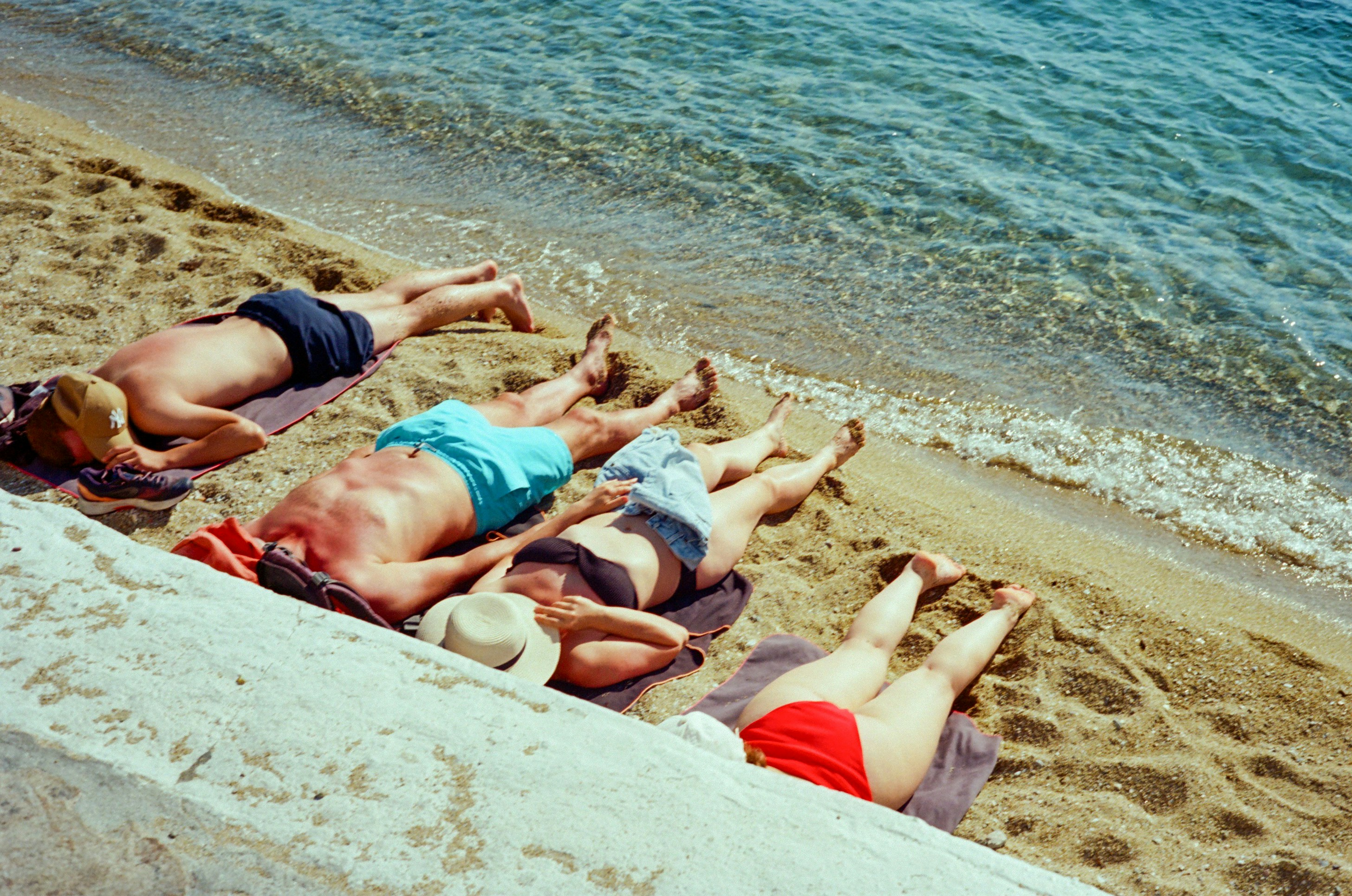 Four people sunbathing on a sandy beach by the ocean.
