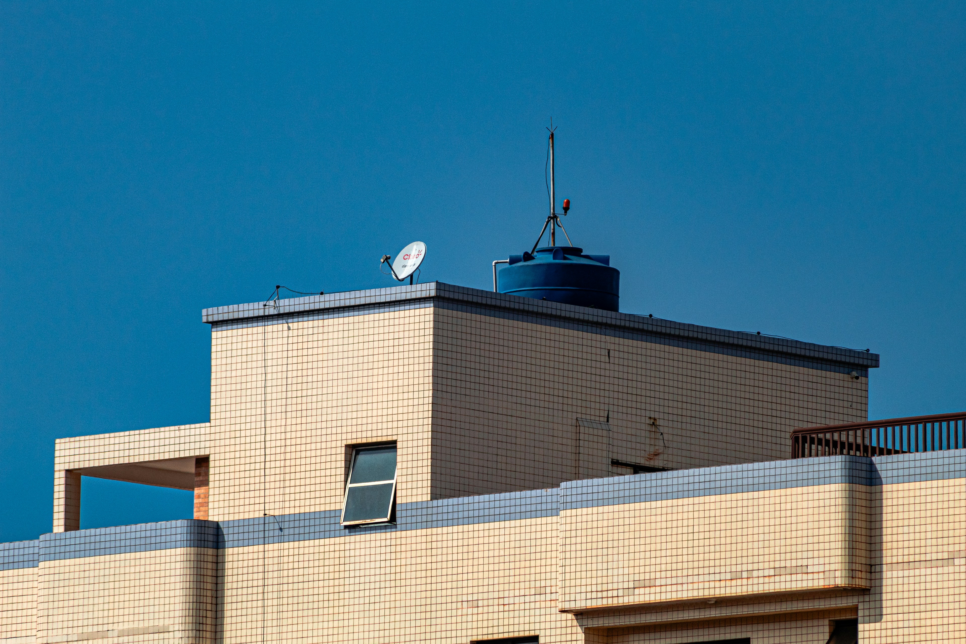 Modern building rooftop with satellite dish and blue water tank.
