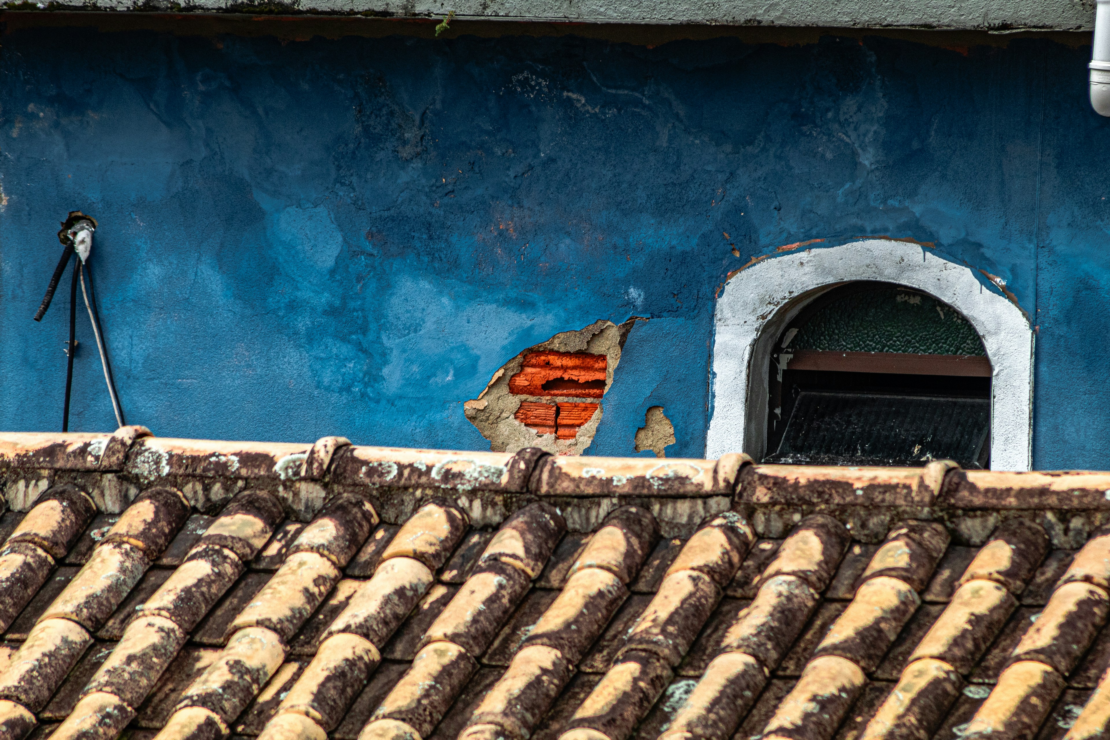 Weathered blue wall, arched window, and terracotta tiled roof.