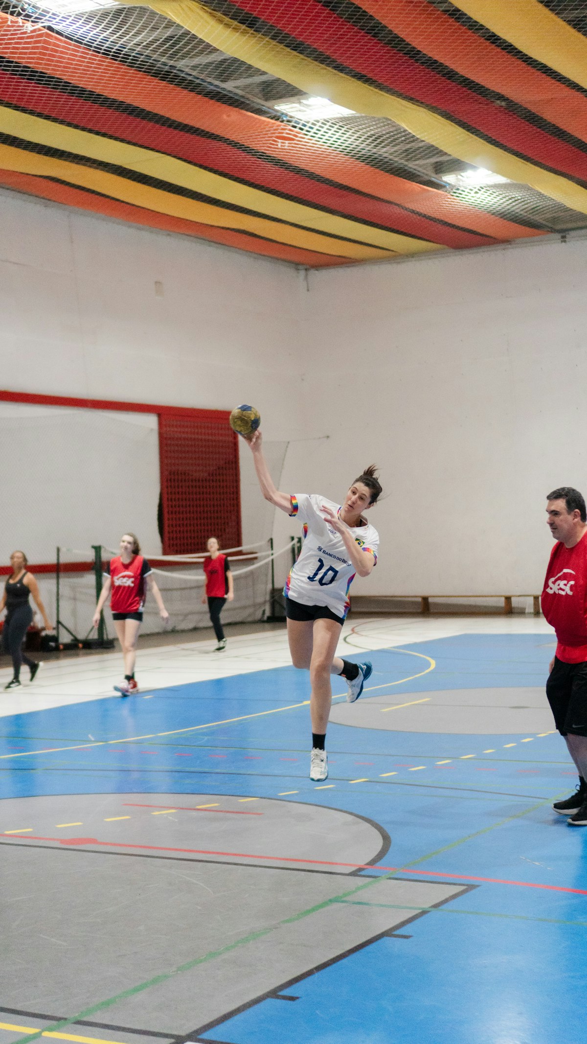 Joueuse de handball en maillot blanc numéro 10 en pleine suspension, bras armé pour tirer, dans un gymnase