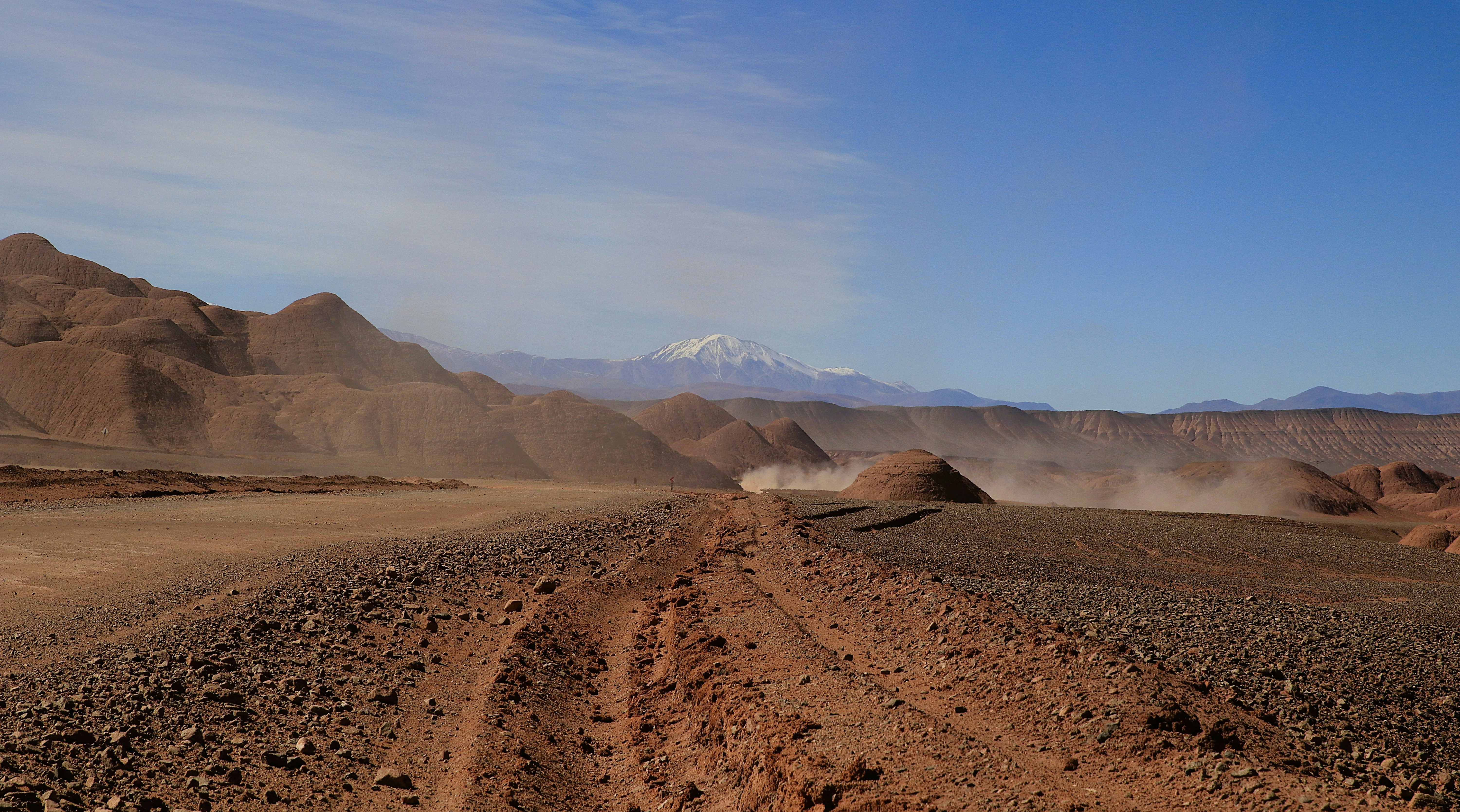 Estrada empoeirada do deserto levando para montanhas cobertas de neve sob céu azul.
