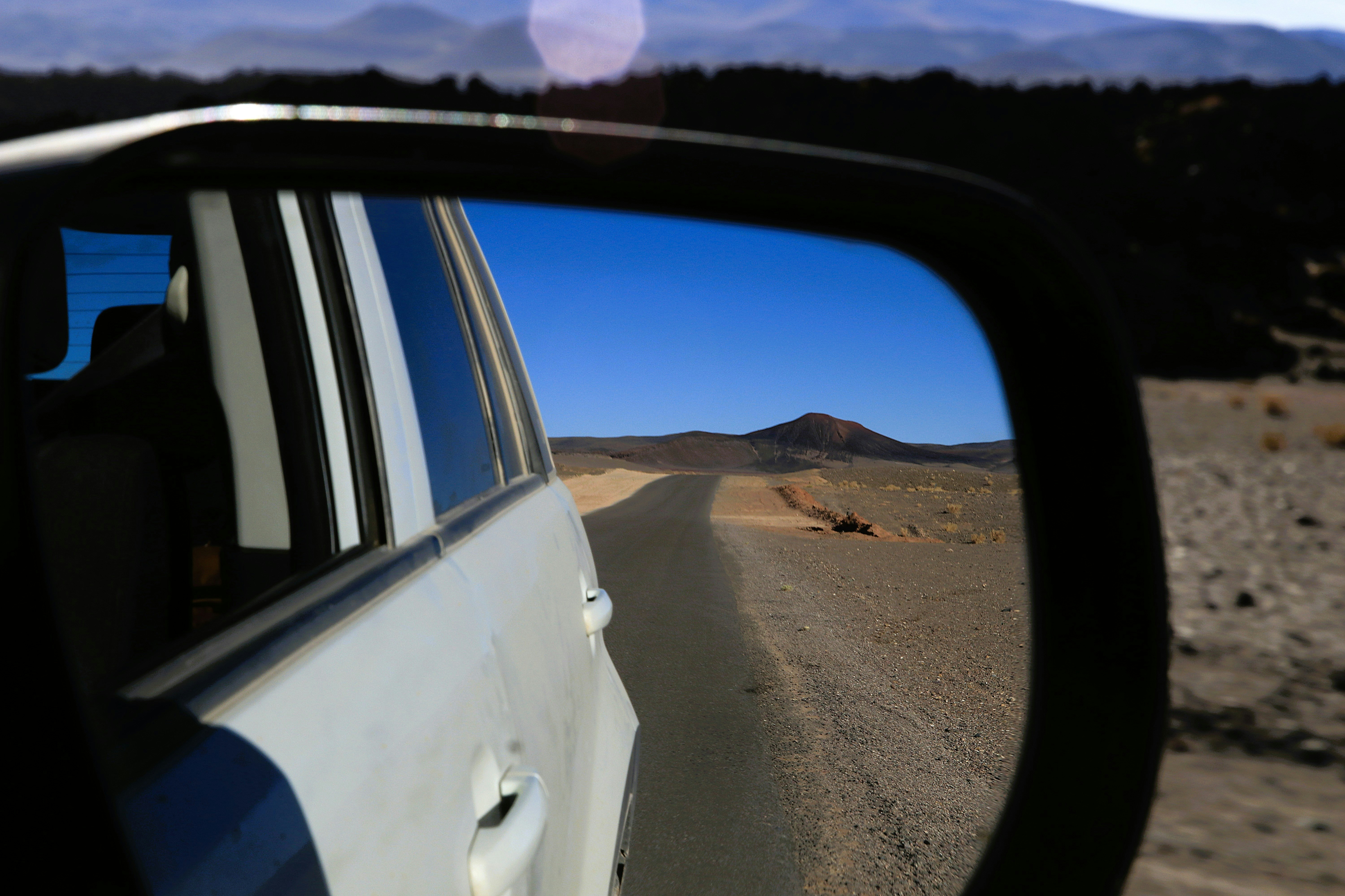 Le rétroviseur latéral de la voiture reflétant une route désertique et des montagnes lointaines.