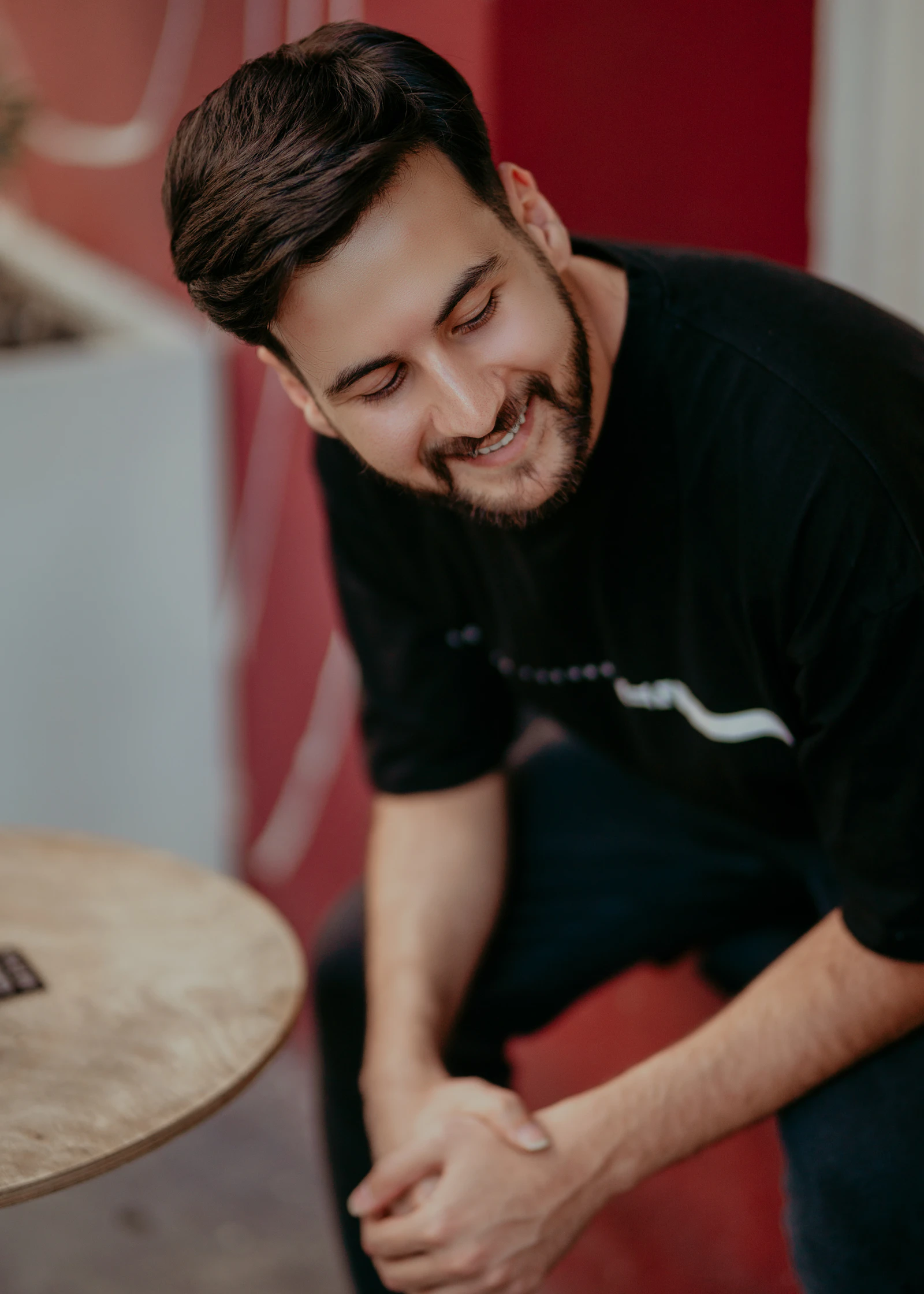 A smiling young man in a black T-shirt sitting and looking down