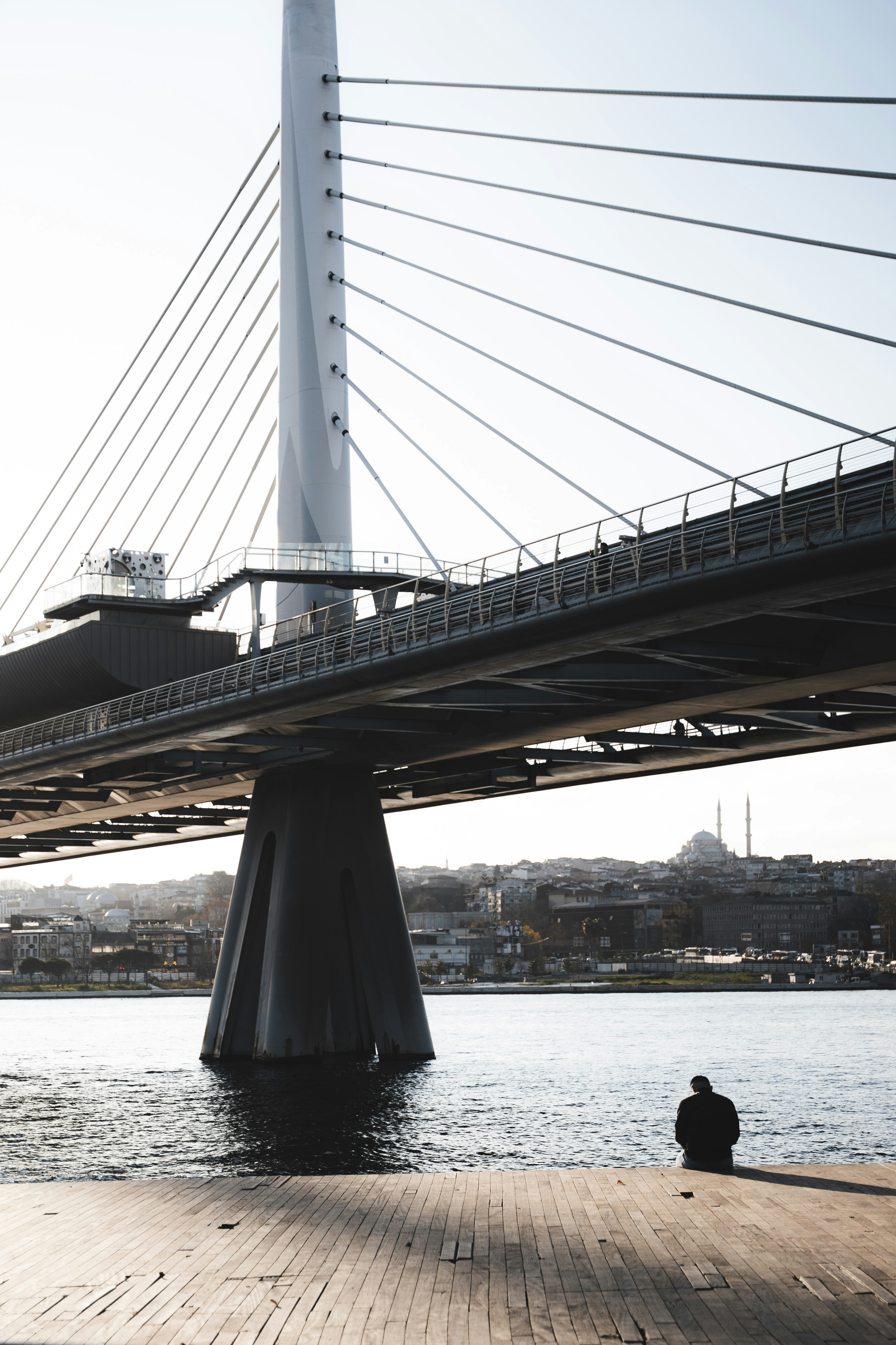 Person sitting by water under istanbul bridge