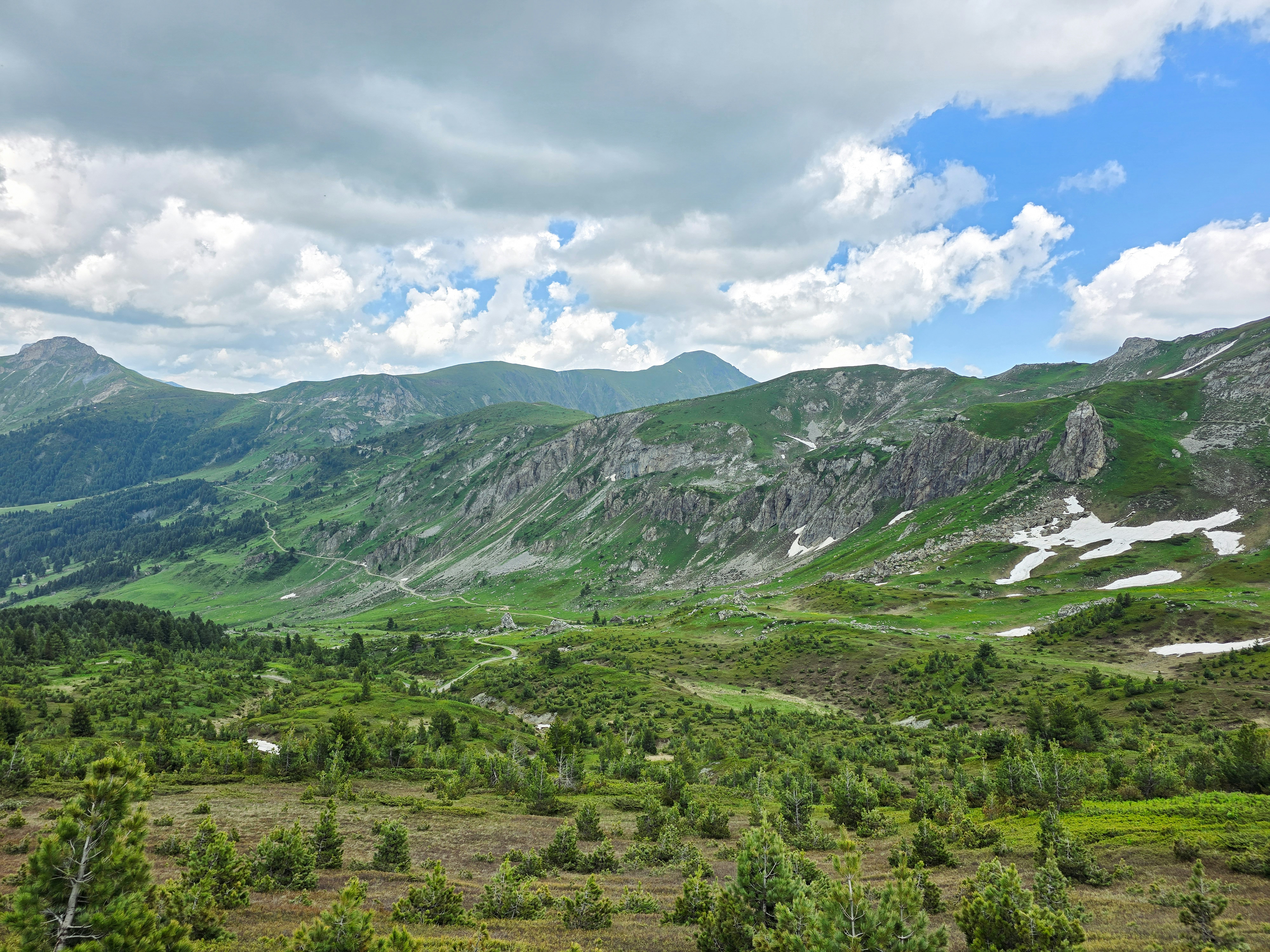 Vast green mountain landscape with rocky terrain and snow.