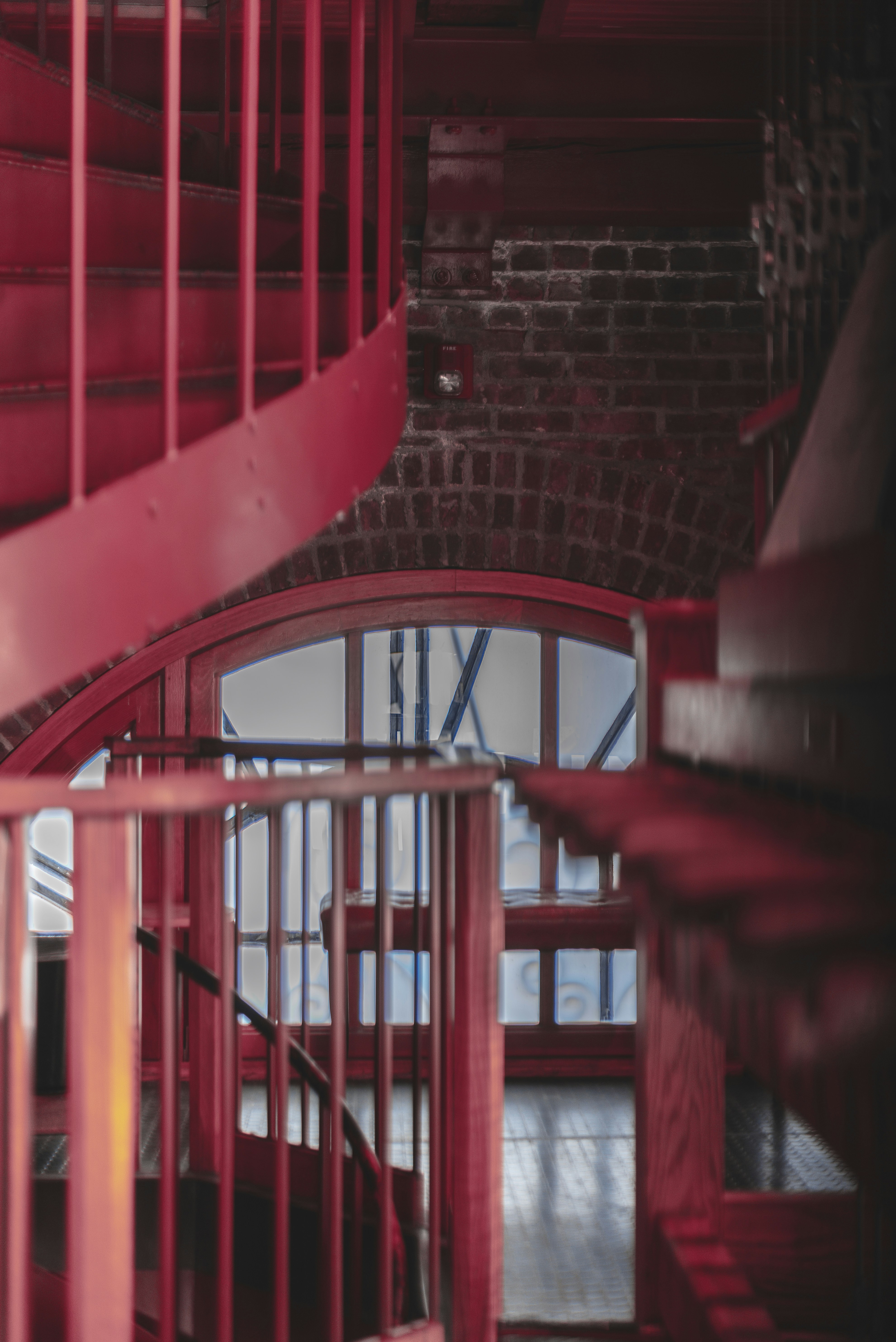 A vibrant red spiral staircase descends towards a window.