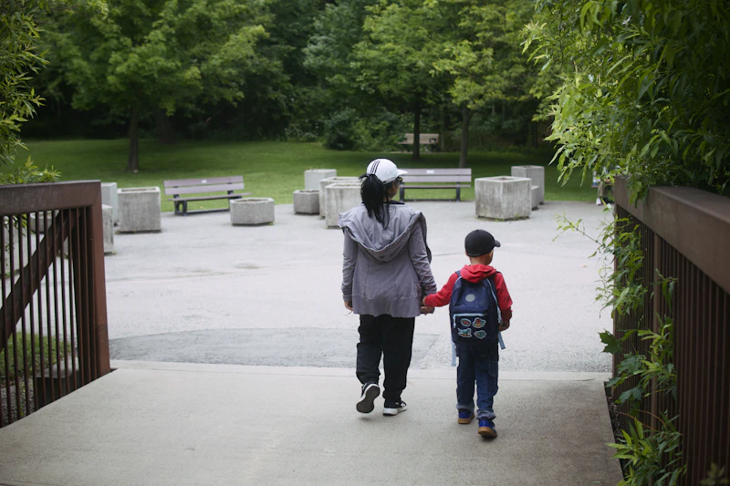 A woman and a young child walking away hand in hand along a park path