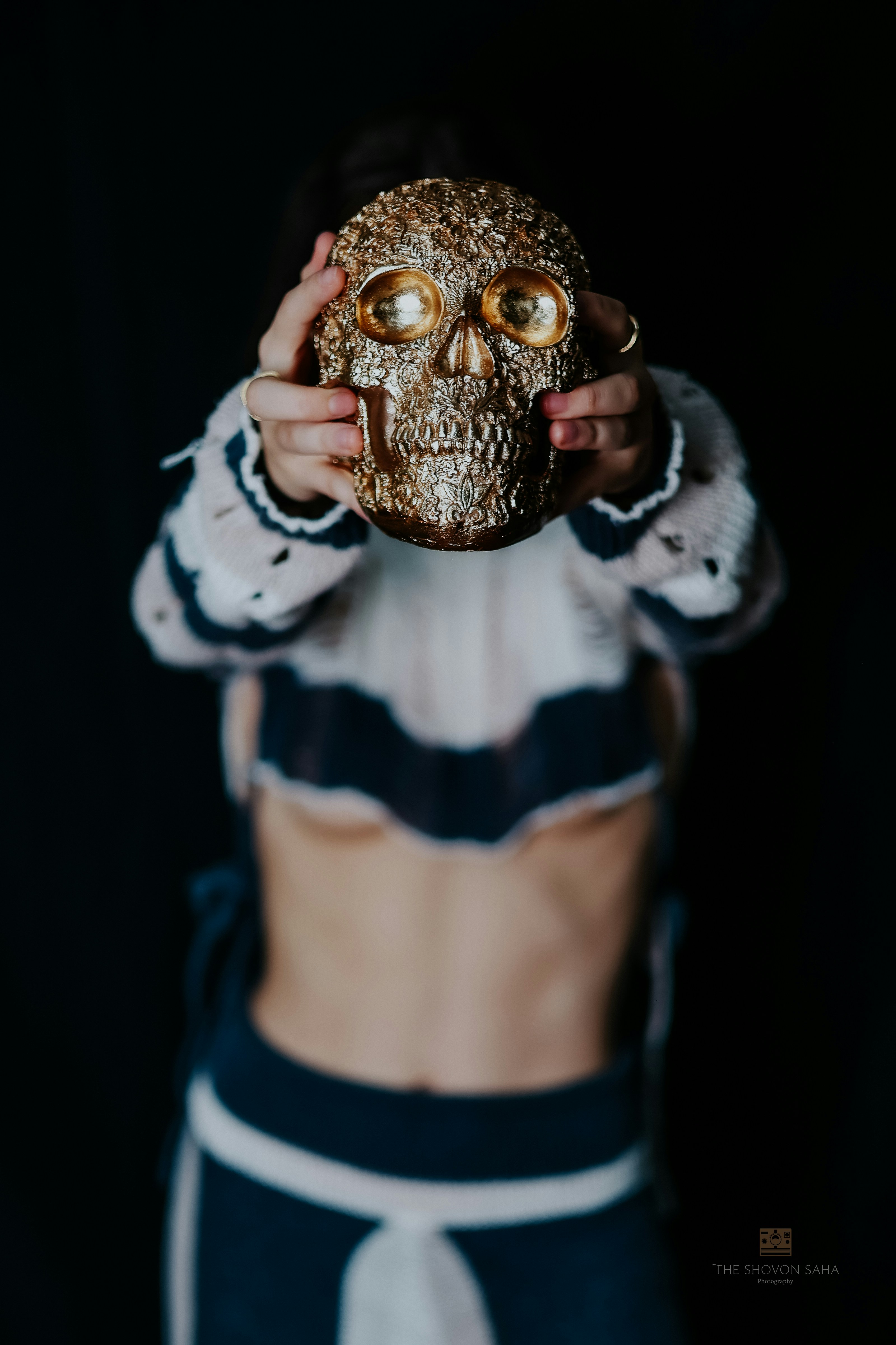A person holding a textured gold skull in front of their face