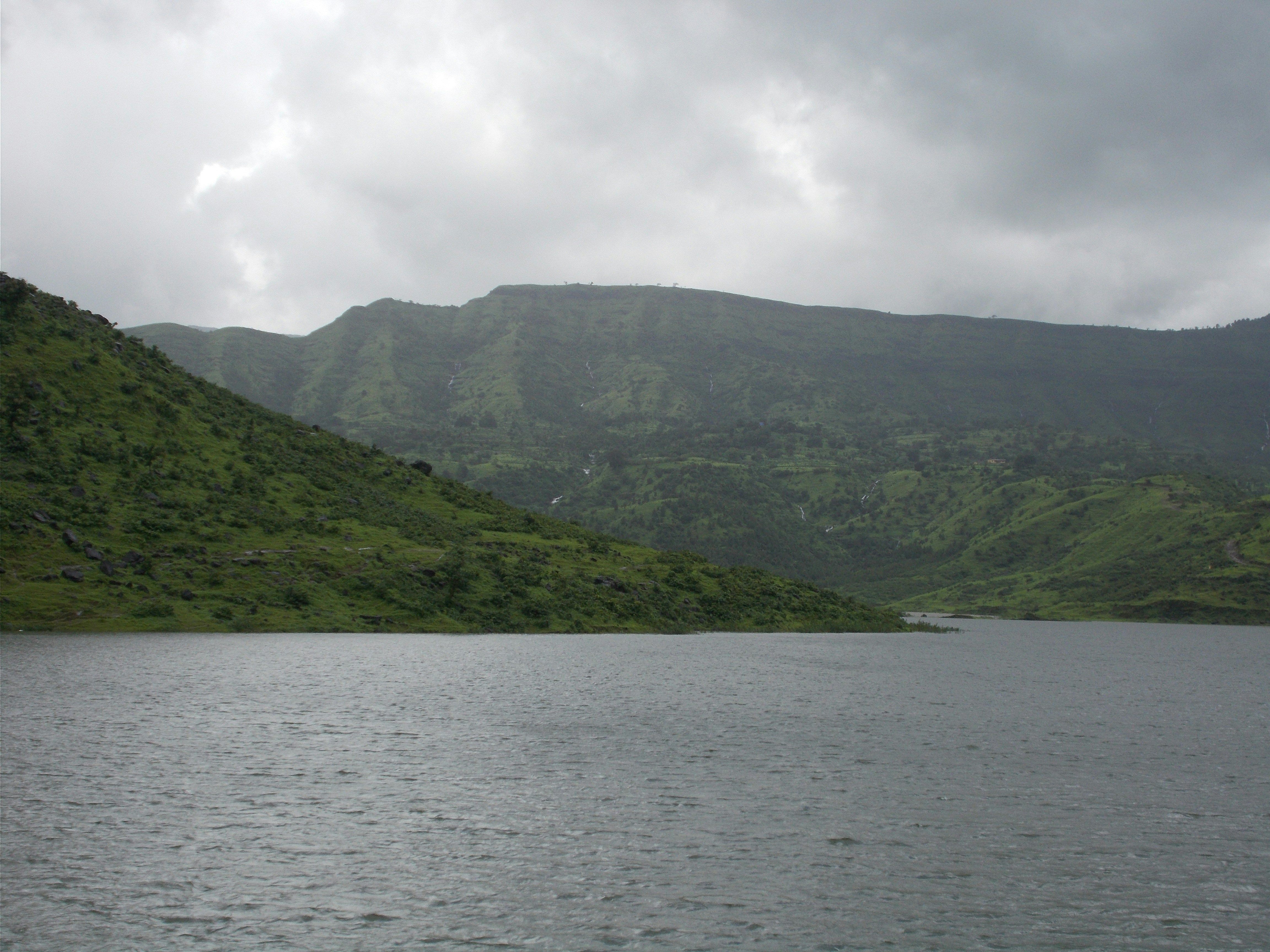 Serene lake with lush green mountains under a cloudy sky.