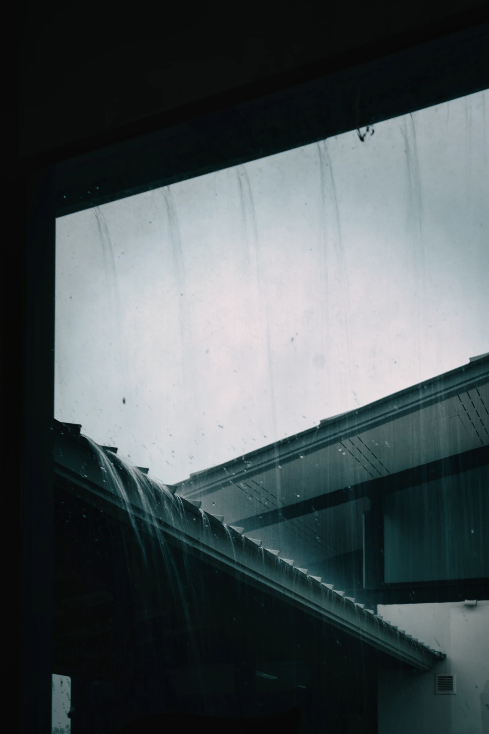 Rainwater overflowing a clogged gutter and roof edge during a downpour