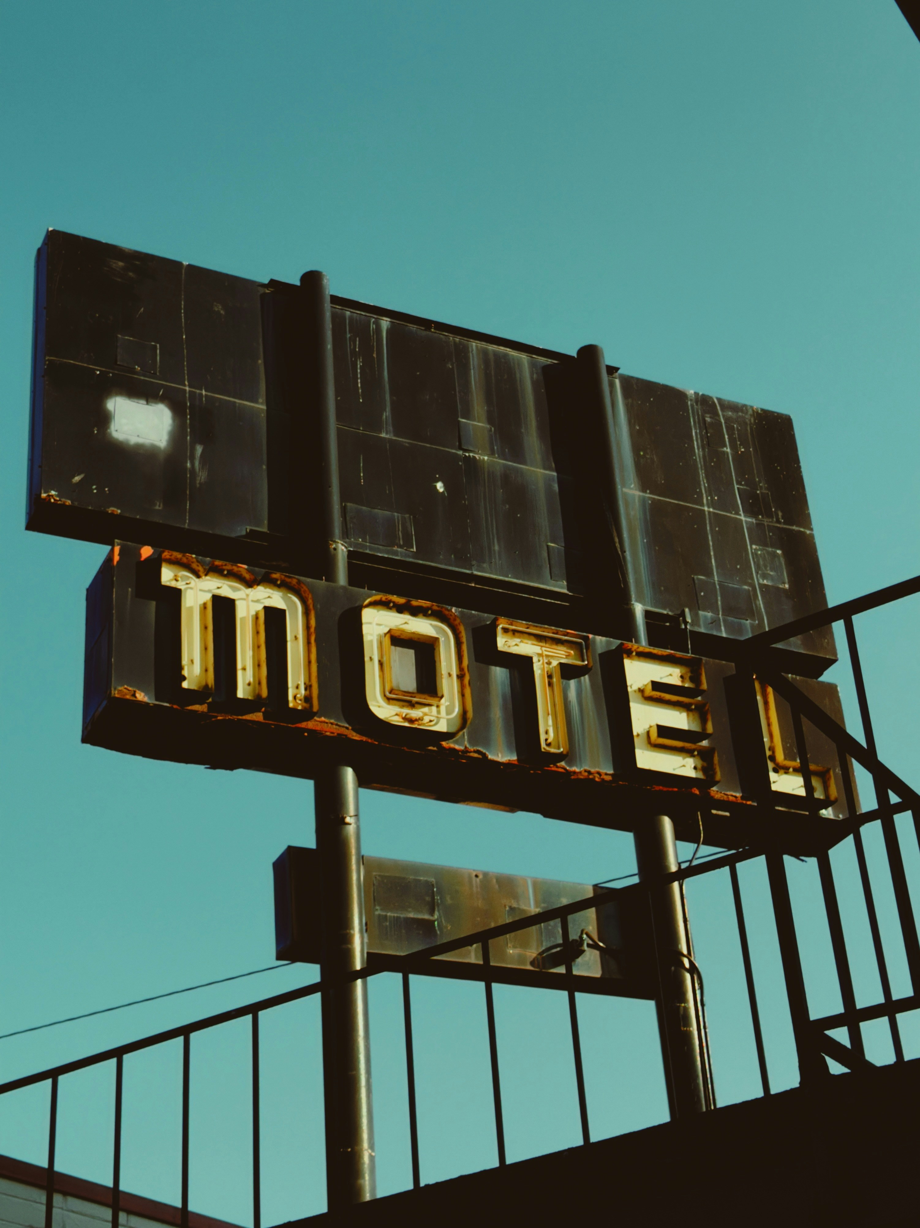 Old, rusty motel sign against a clear blue sky.
