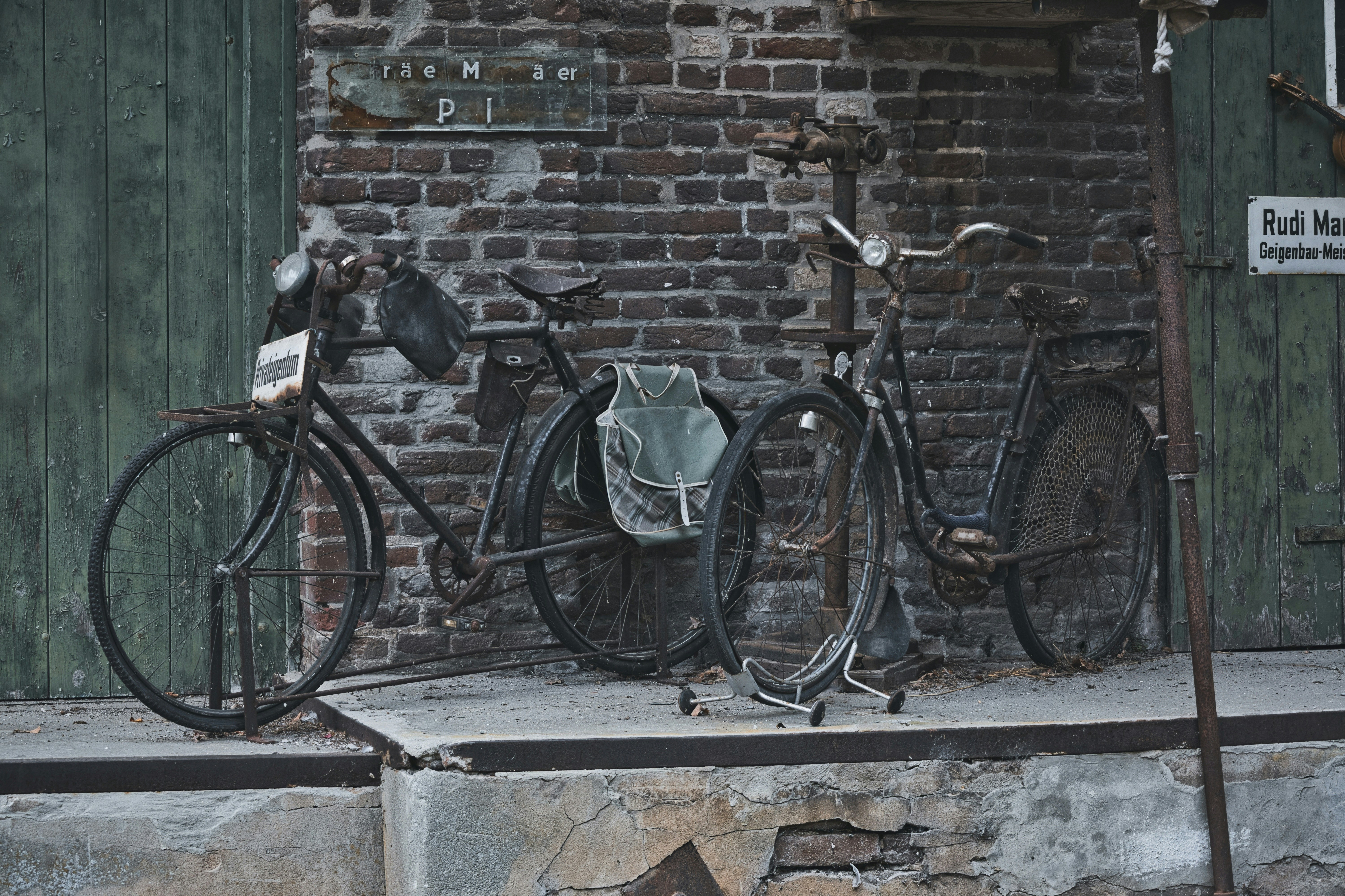 Two old bicycles parked against a rustic brick wall.