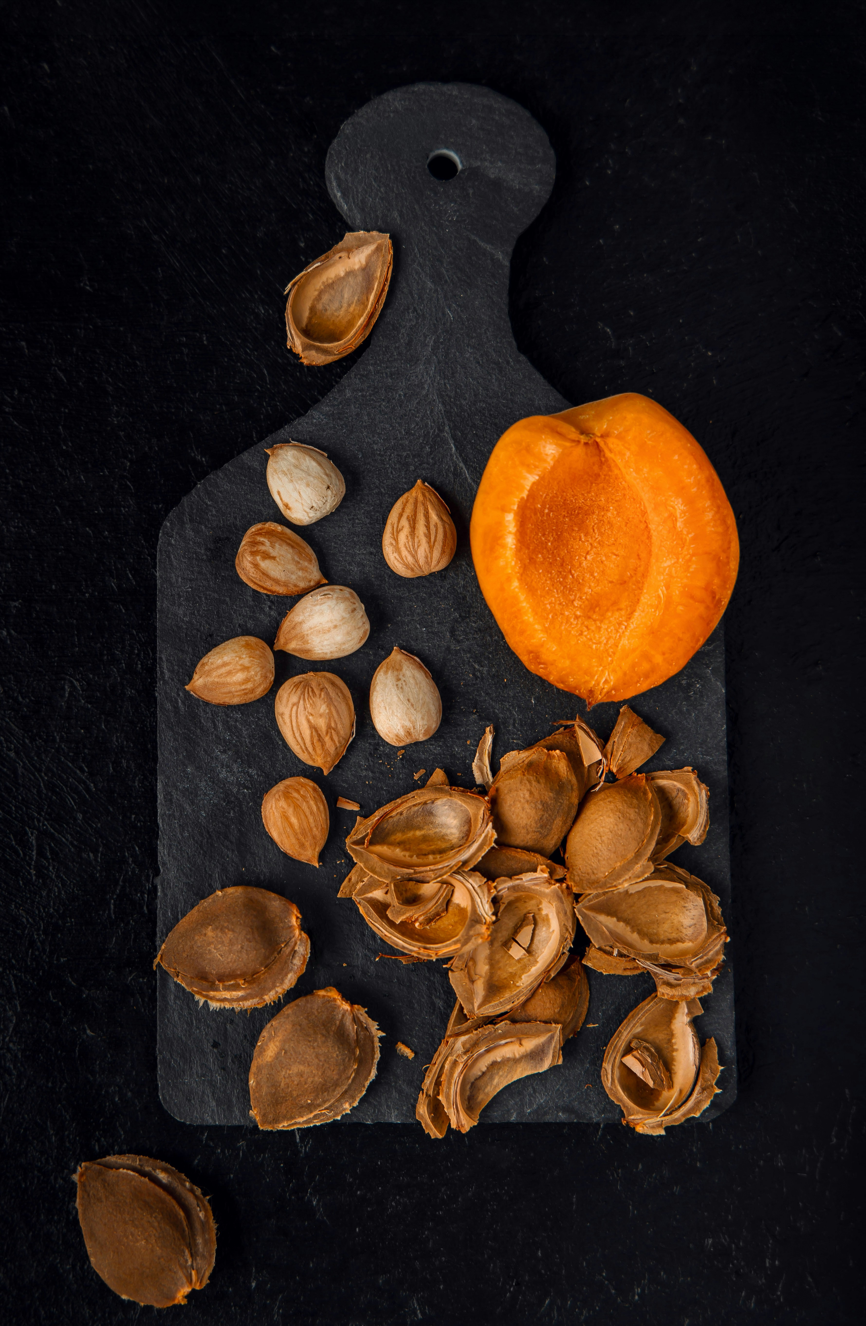 Halved apricot, pits, and shells on a dark cutting board.