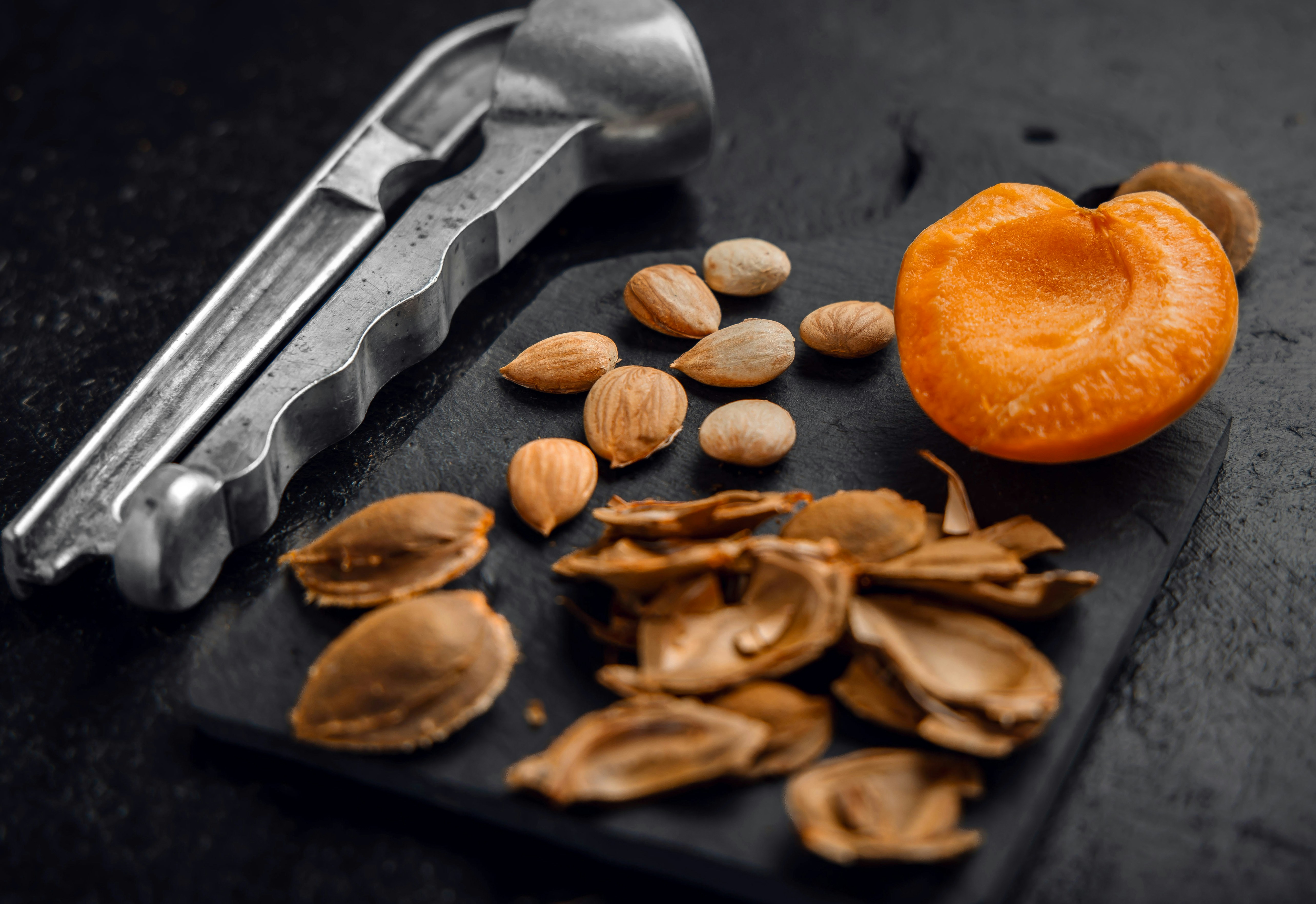 Apricot halves, kernels, shells, and nutcracker on dark surface.