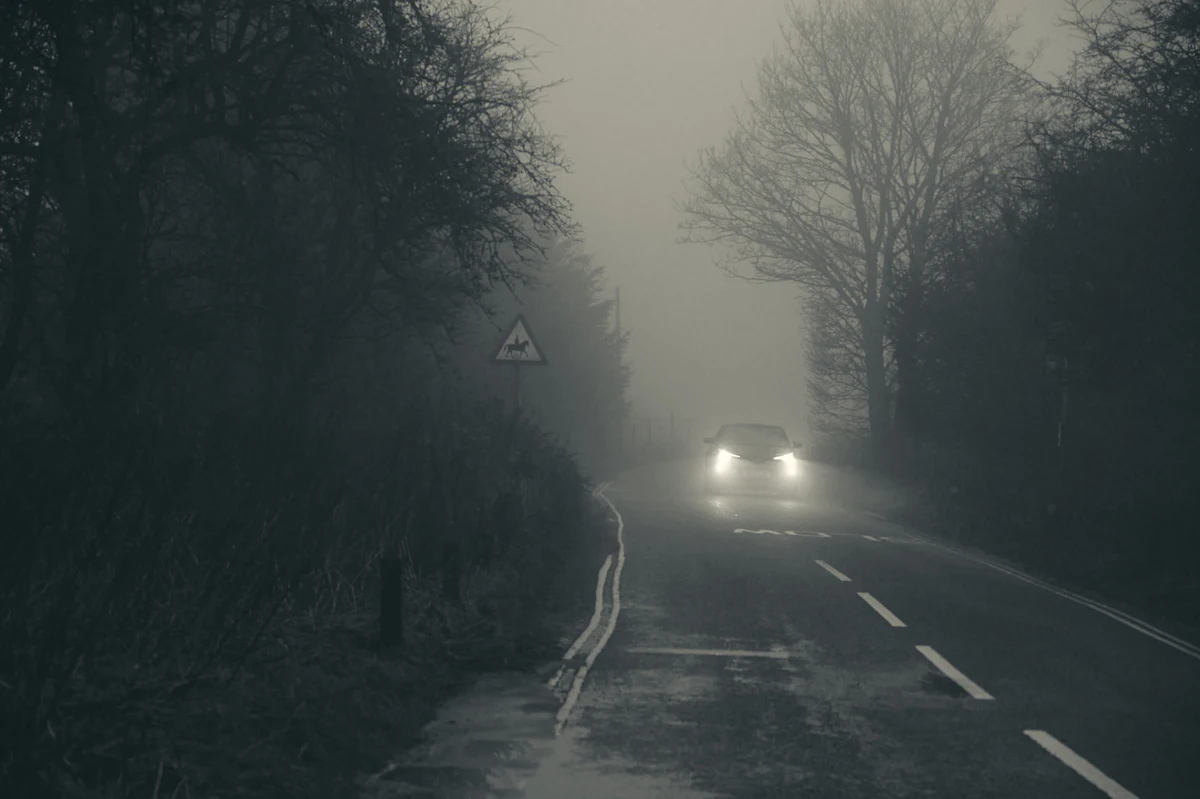 Headlights coming through fog past a warning sign