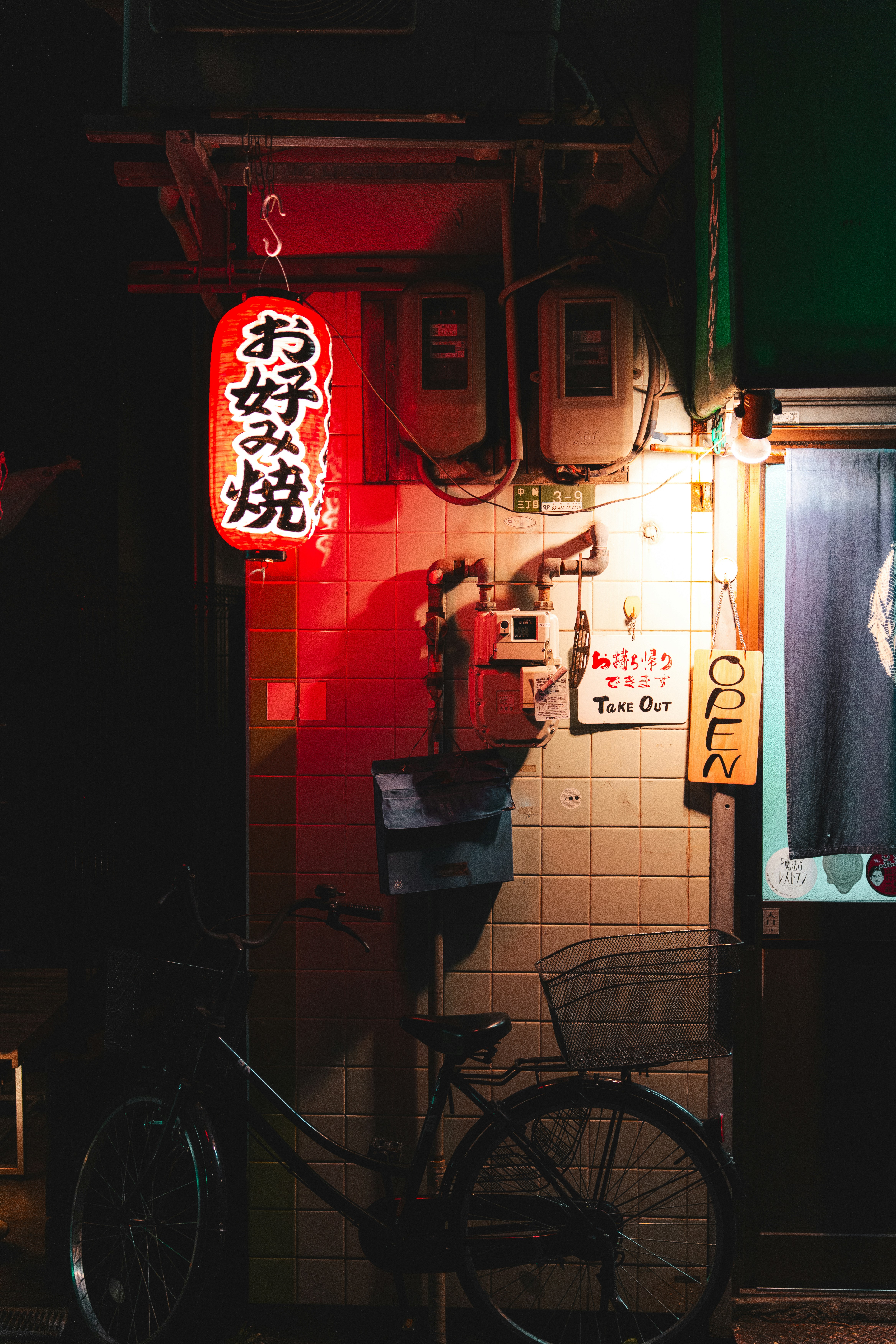 Red japanese lantern illuminates bicycle parked outside building at night.