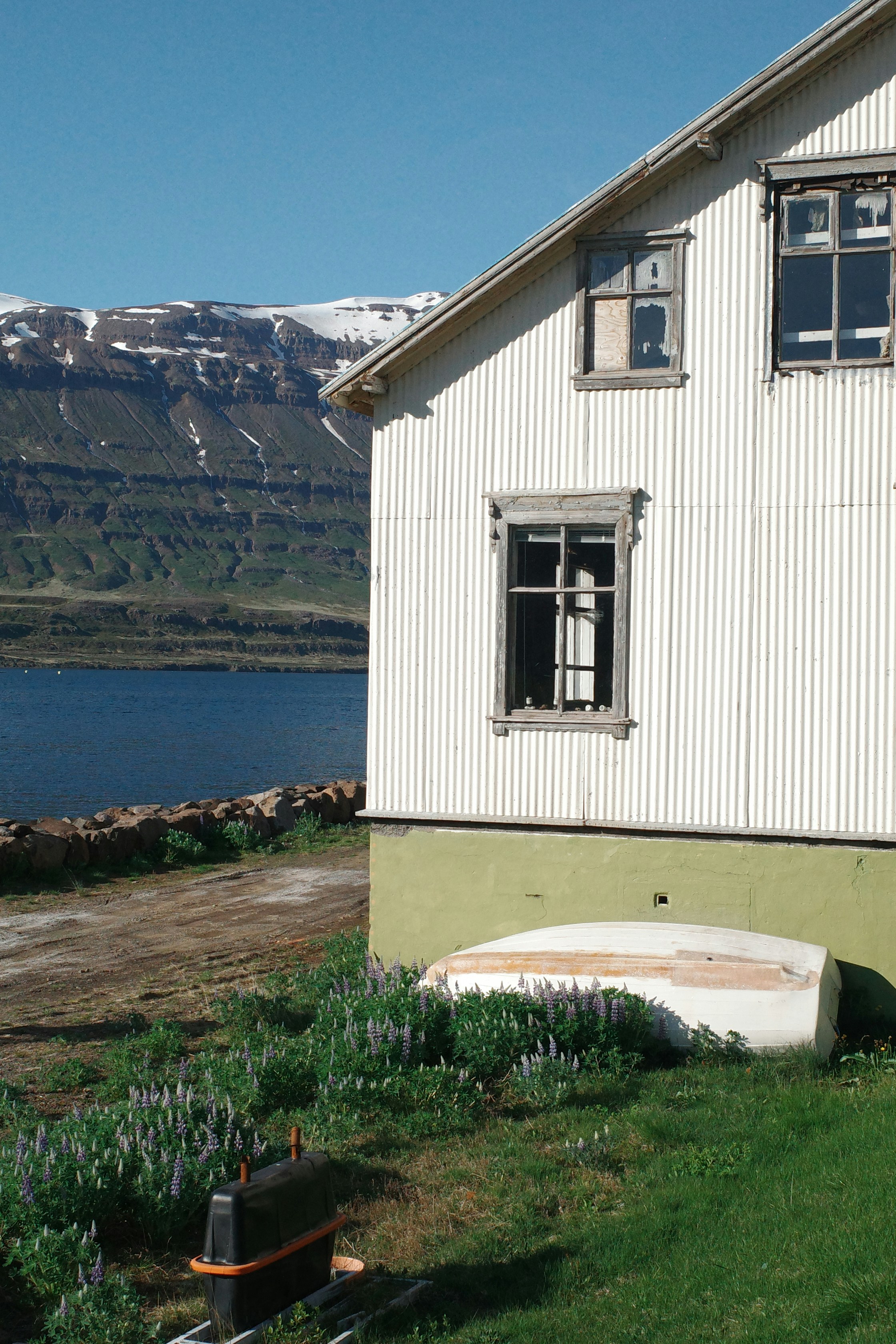 Maison blanche avec bateau au bord du lac et montagnes enneigées au loin.