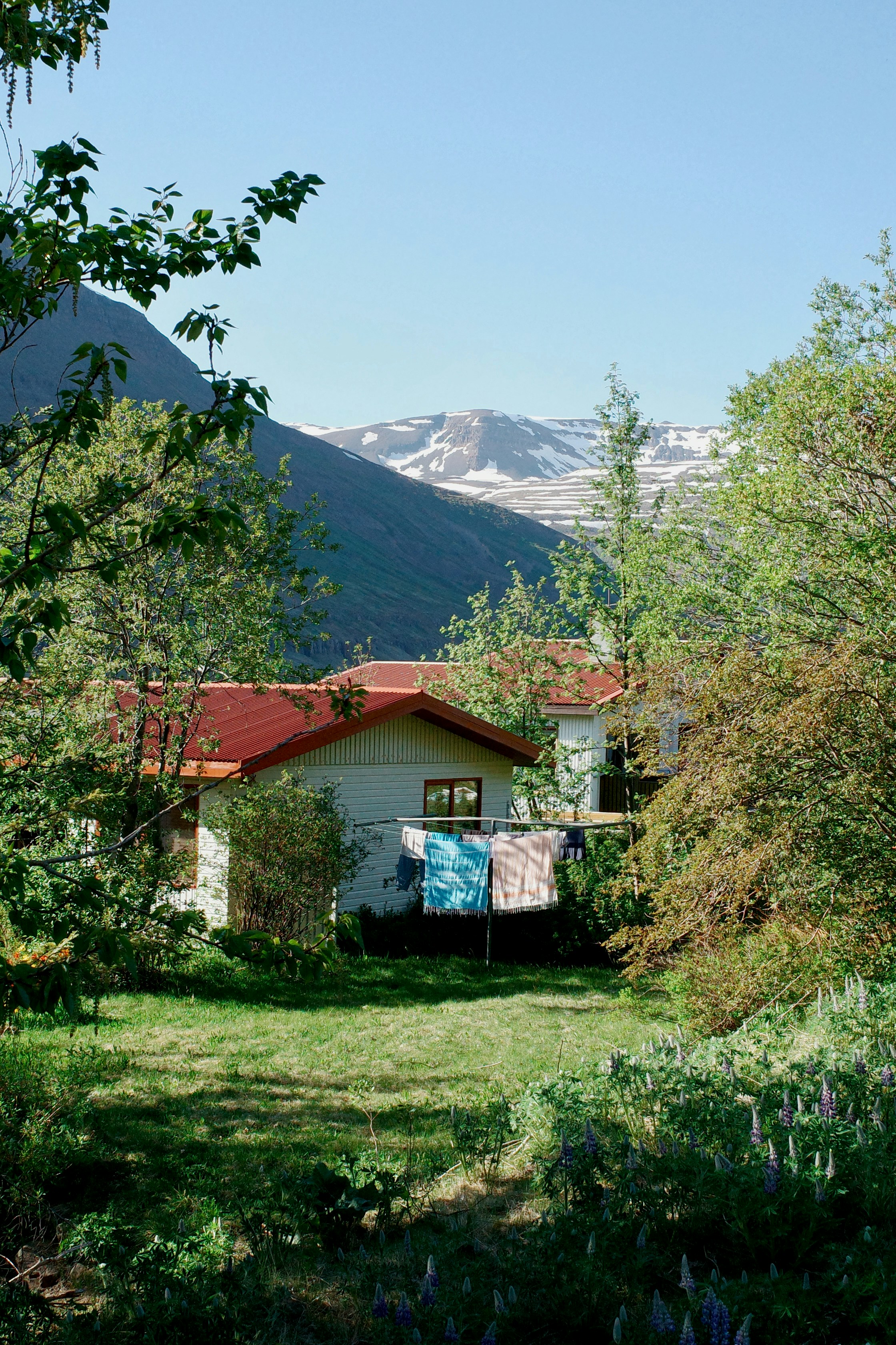 Maison rurale au toit rouge, blanchisserie et montagnes enneigées.