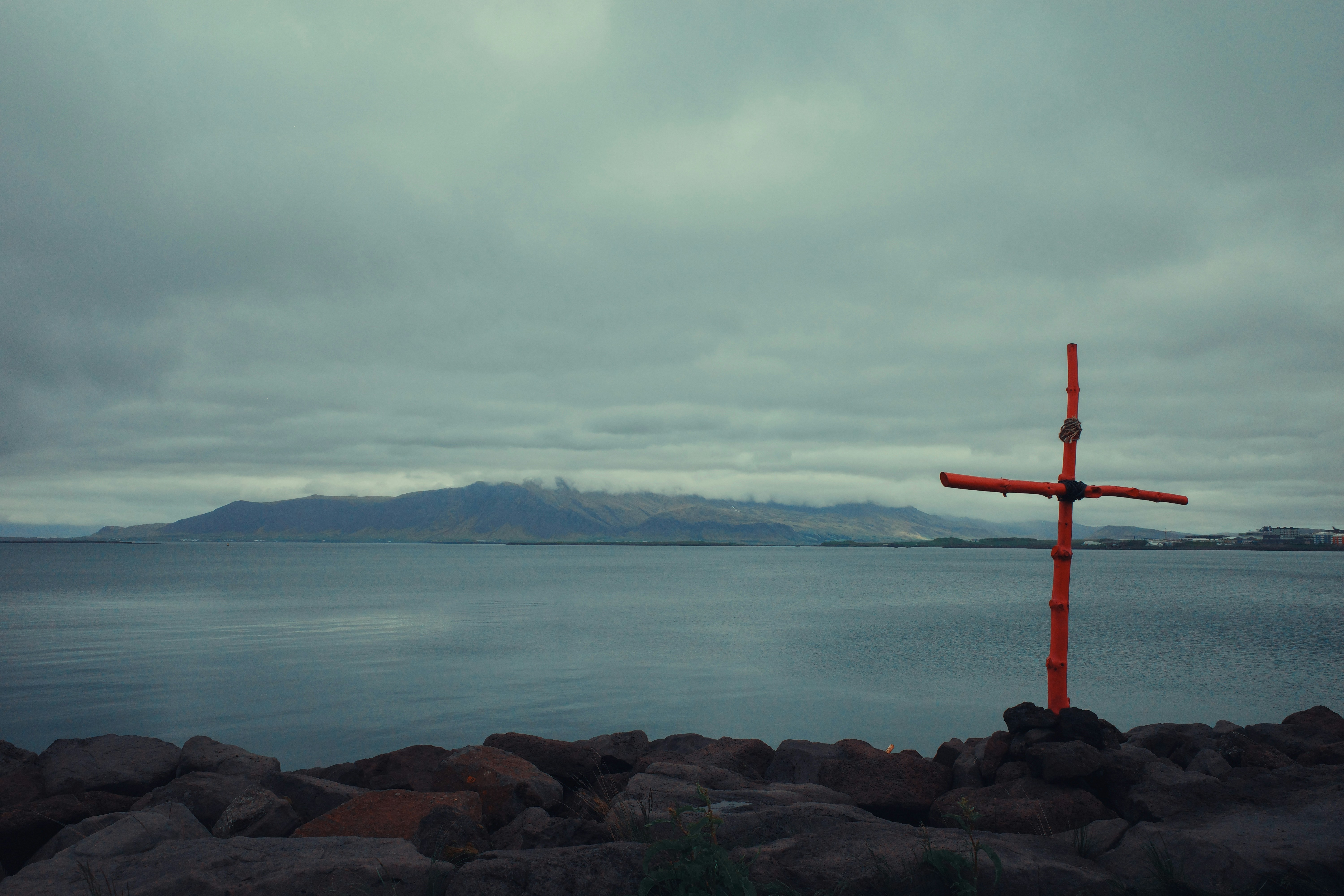 Croix rouge sur des rochers près d’eaux calmes et de montagnes lointaines.