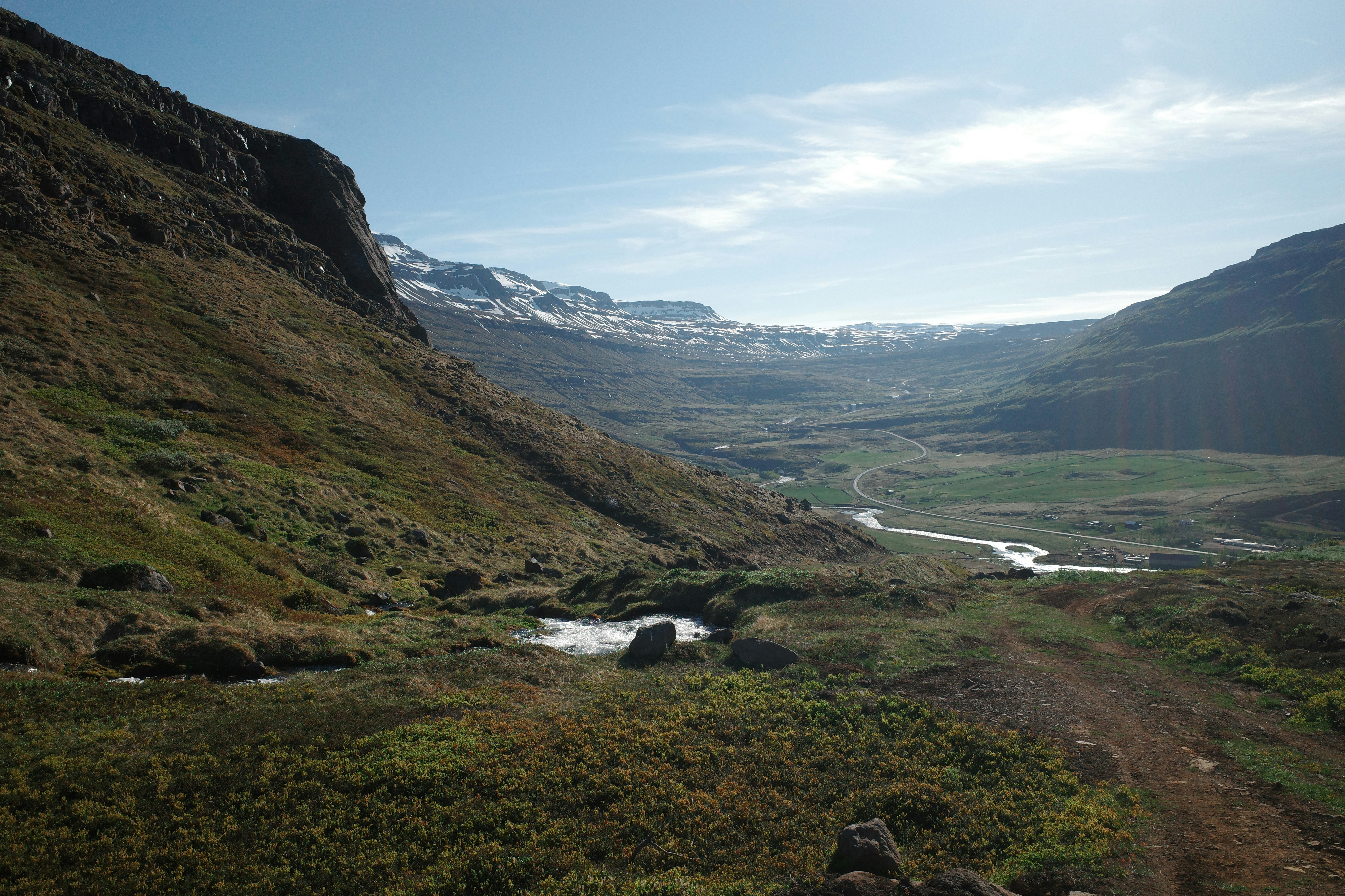 Vallée verte avec une rivière qui s’écoule vers des montagnes enneigées.