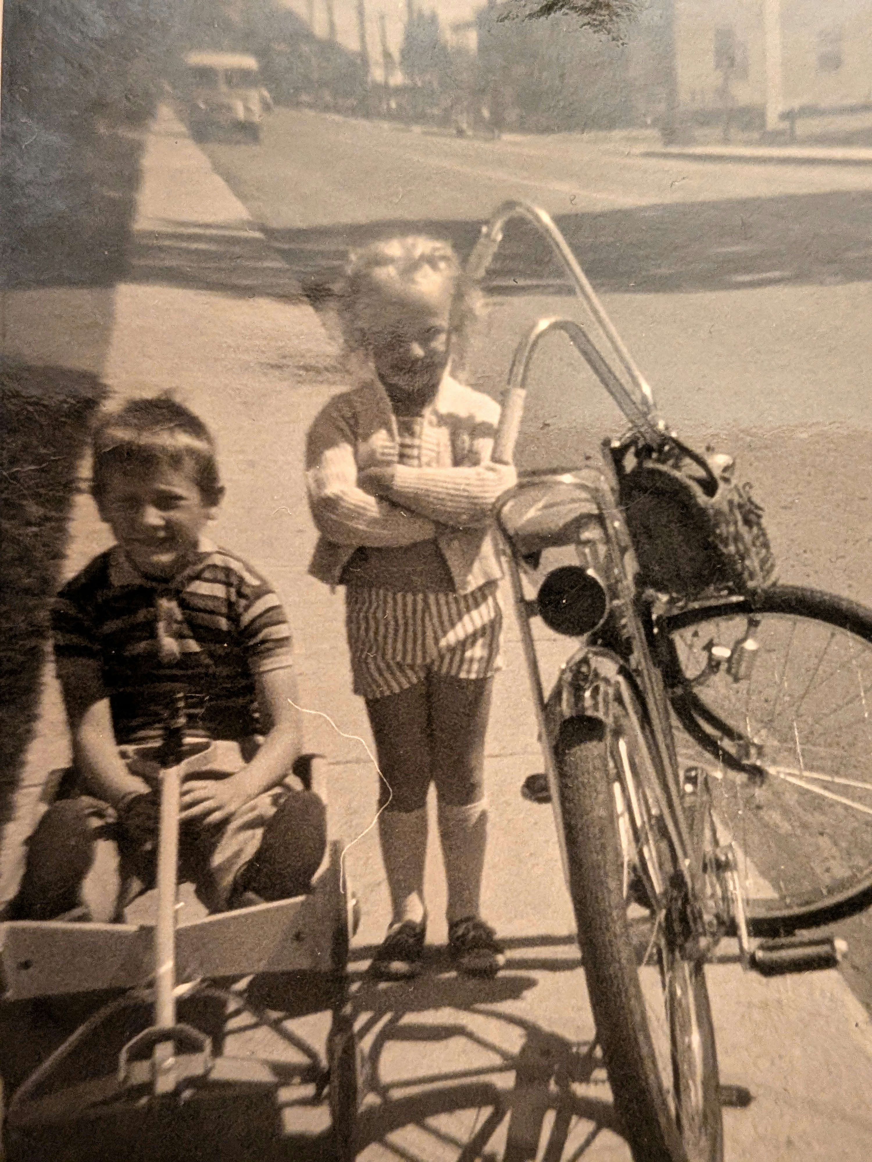Boy in wagon, girl with bicycle on a sunny street.