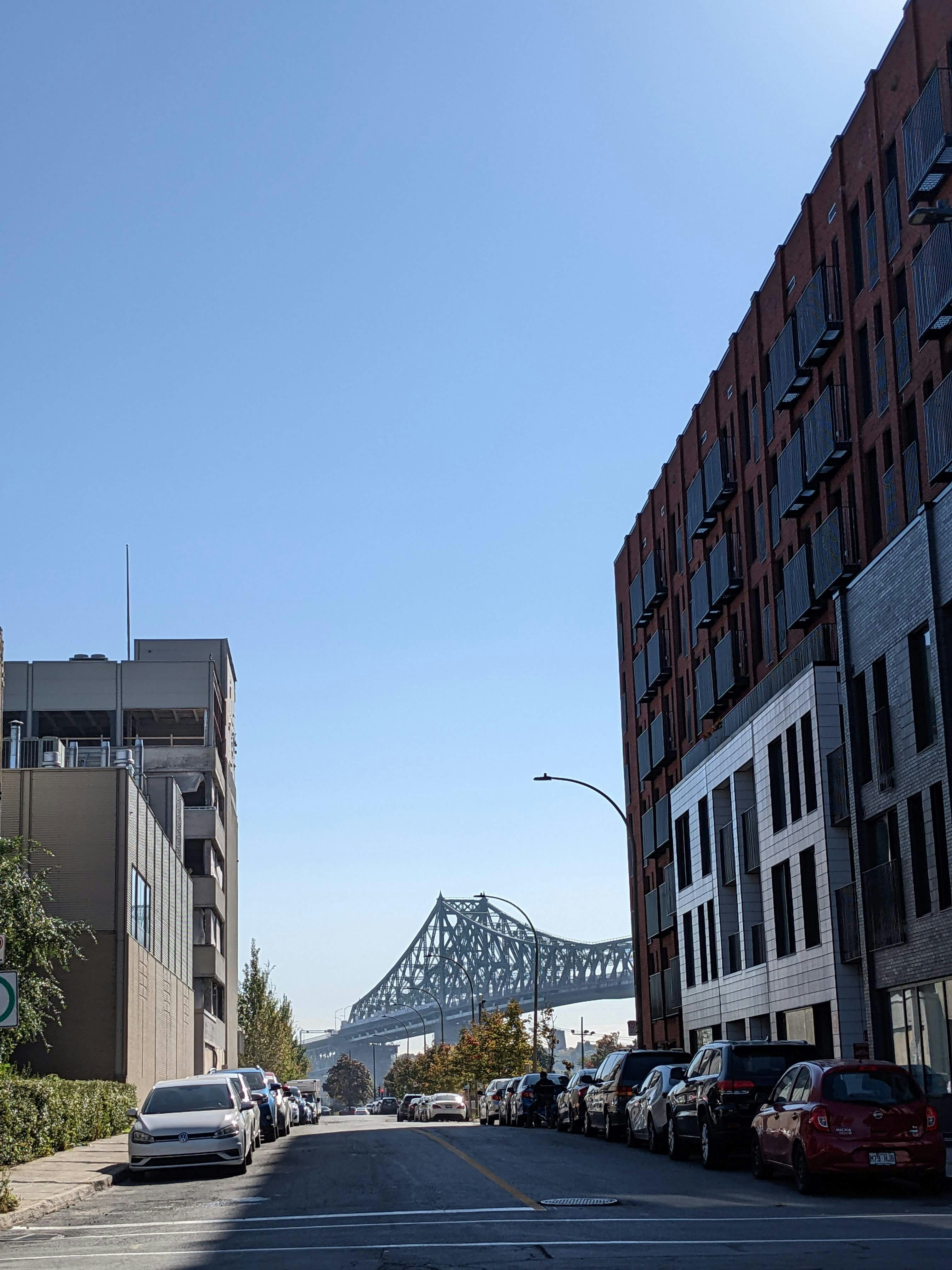City street with buildings leads to a large green bridge.