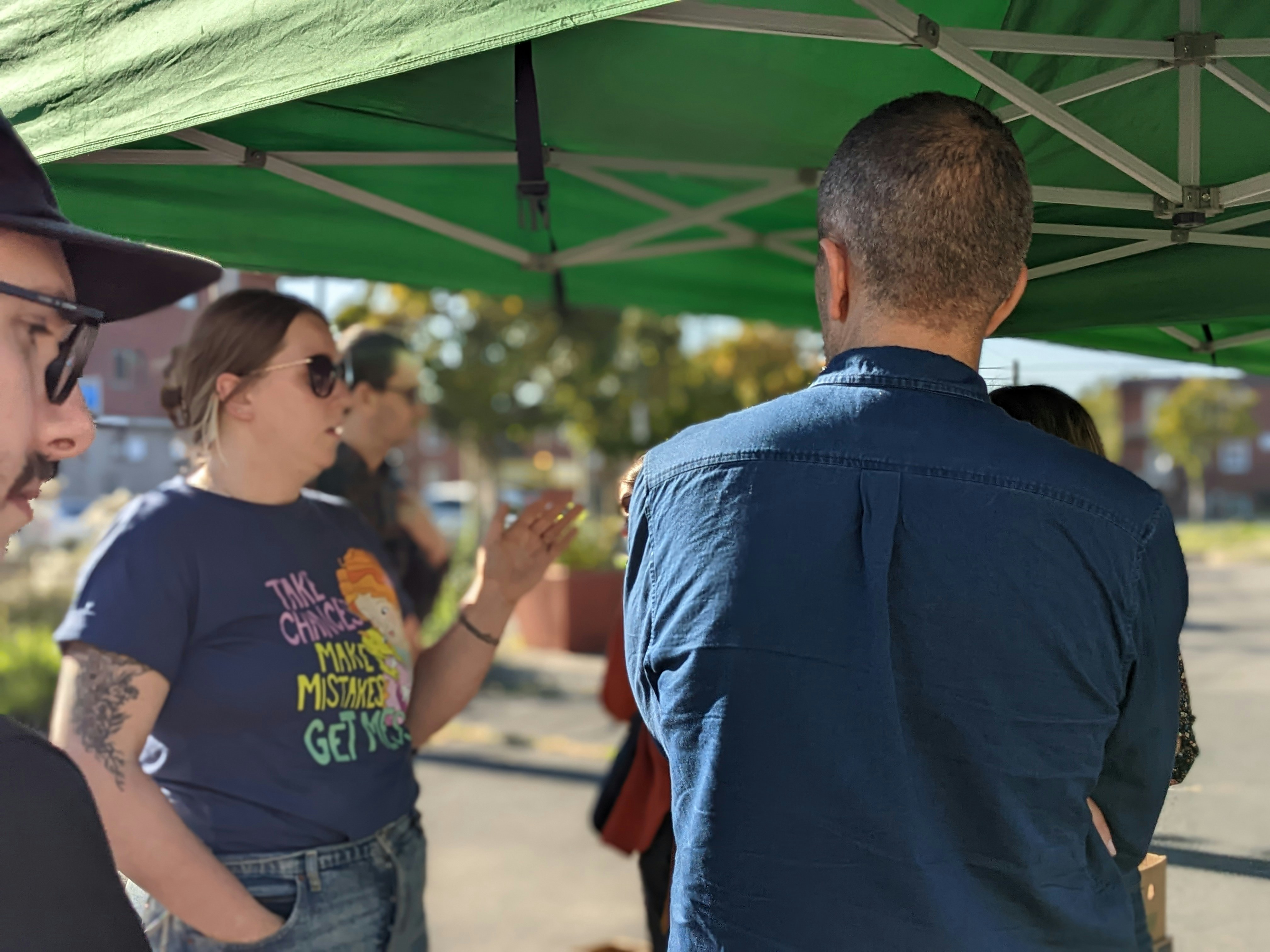 People talking under a green canopy outdoors.