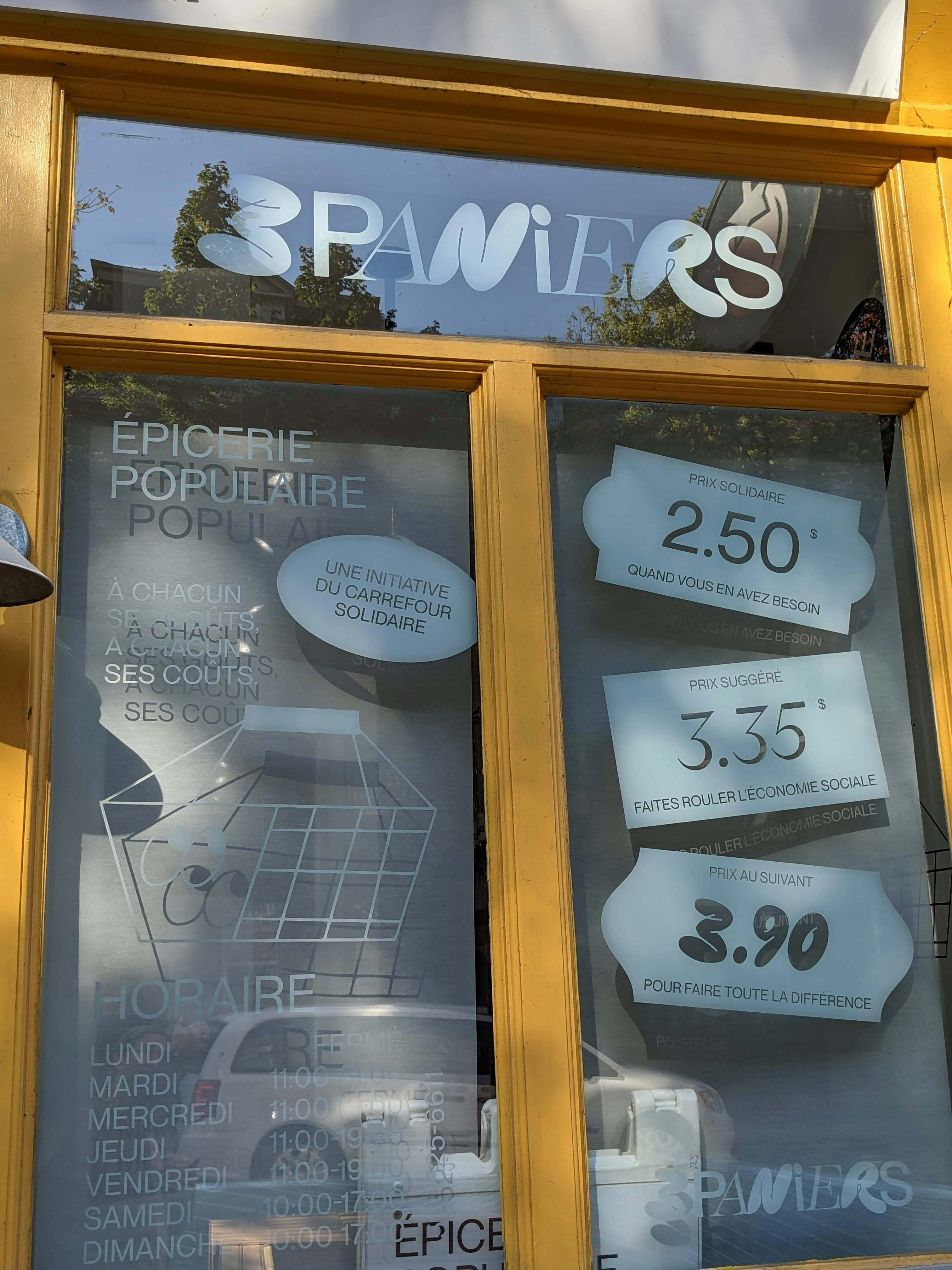 Yellow storefront window with "3 paniers" sign and prices.