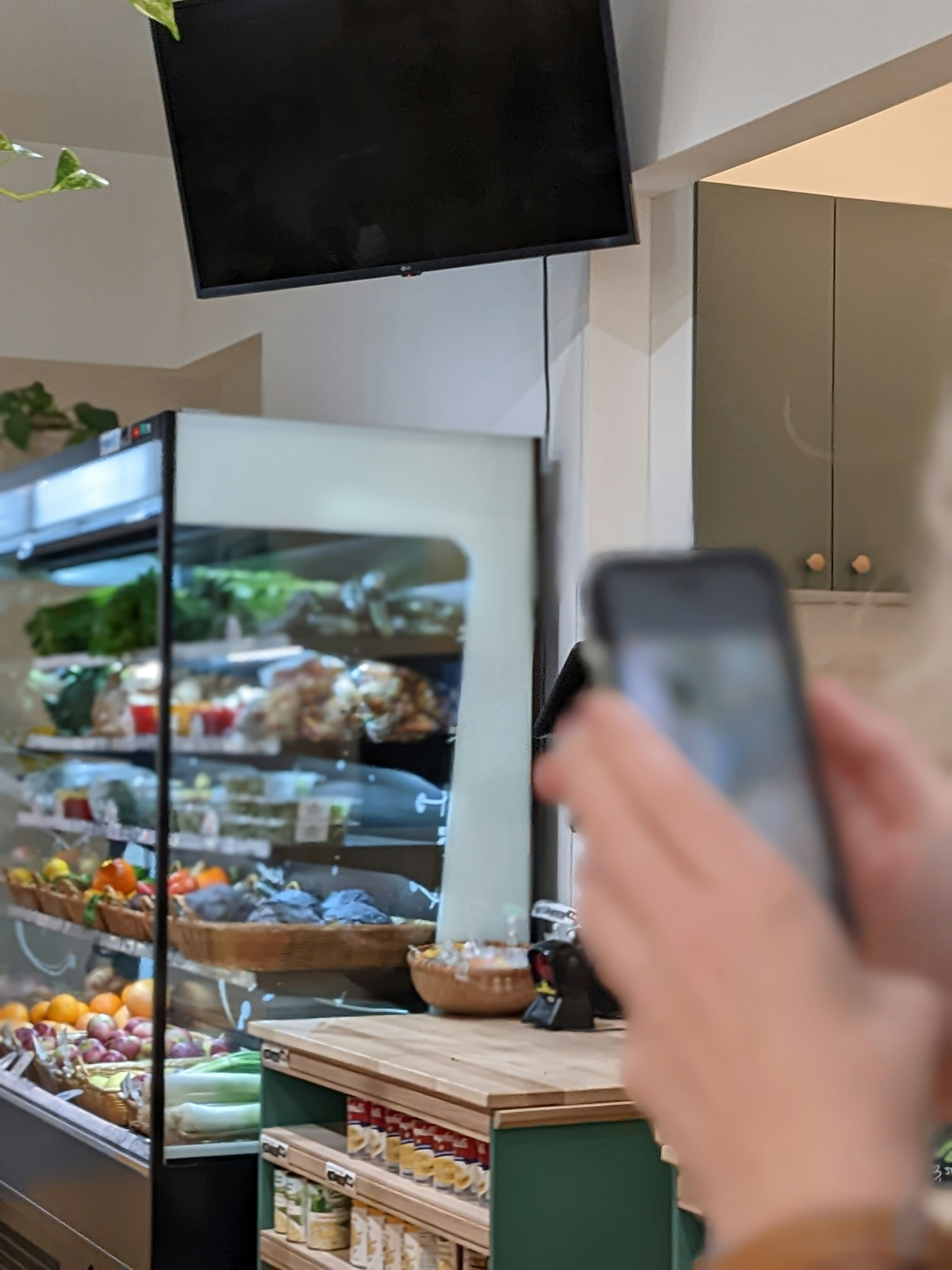 Customer holding phone near a refrigerated fresh food display.
