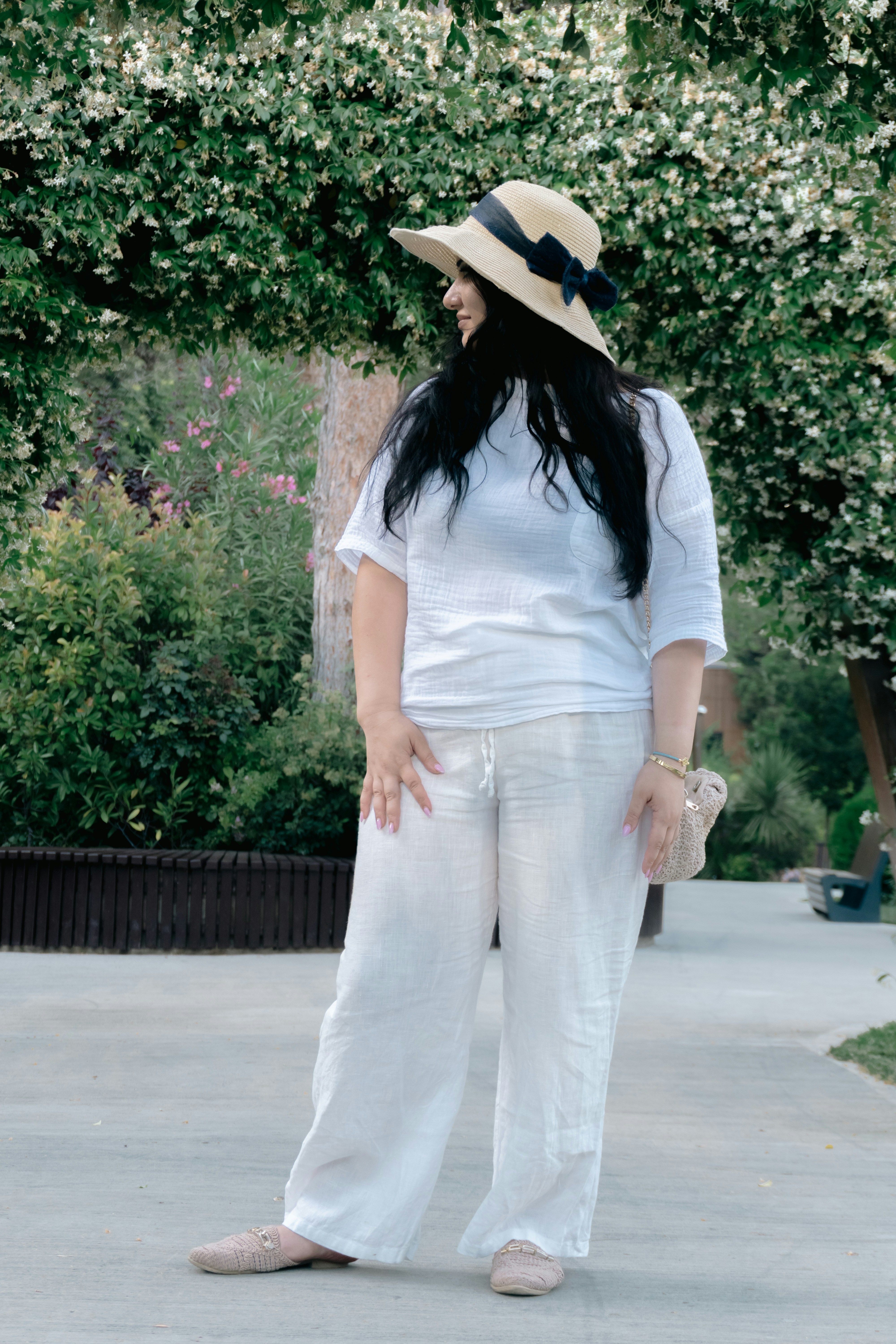 Woman in white linen outfit and straw hat in nature.