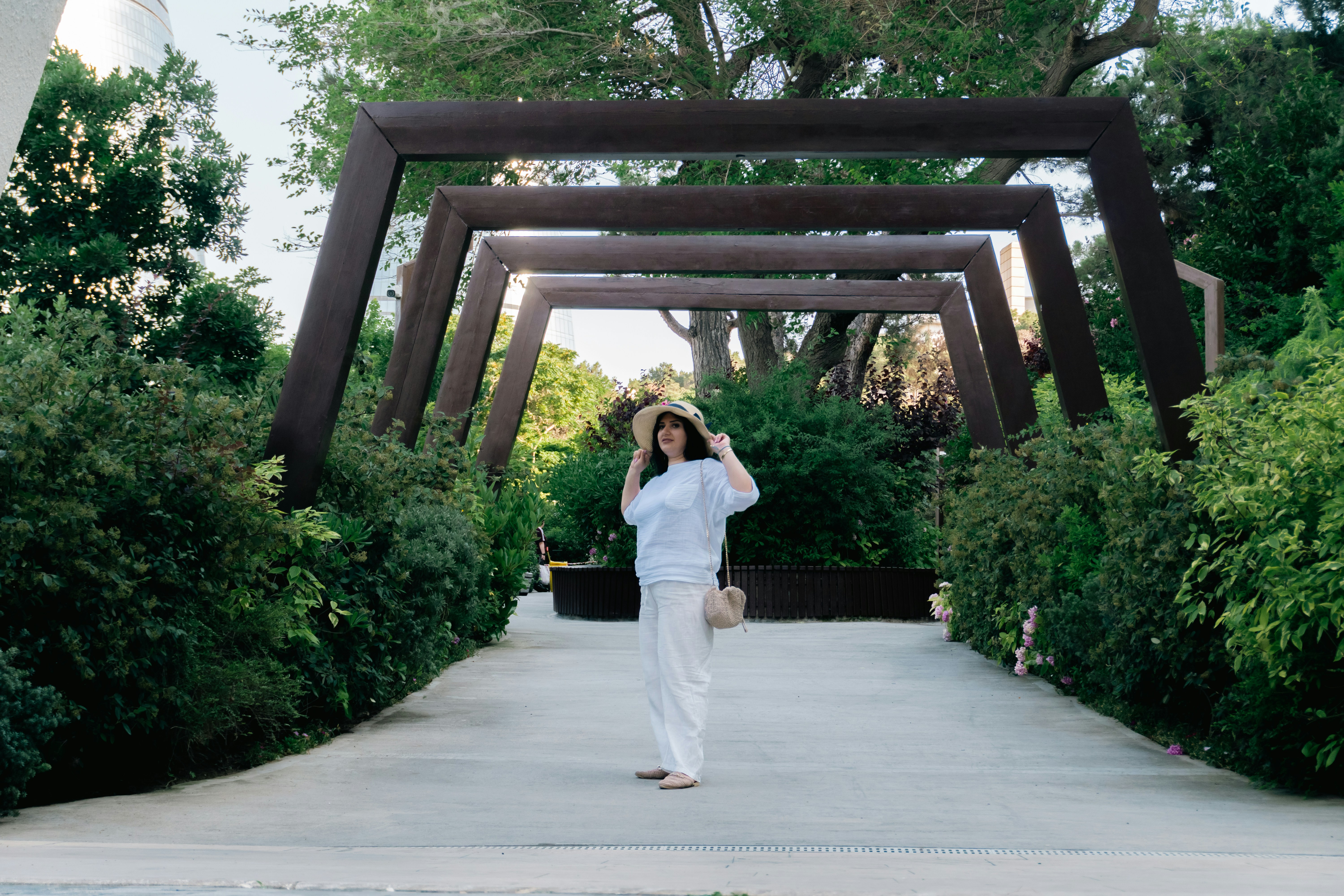 Woman in hat stands on path under geometric archways.