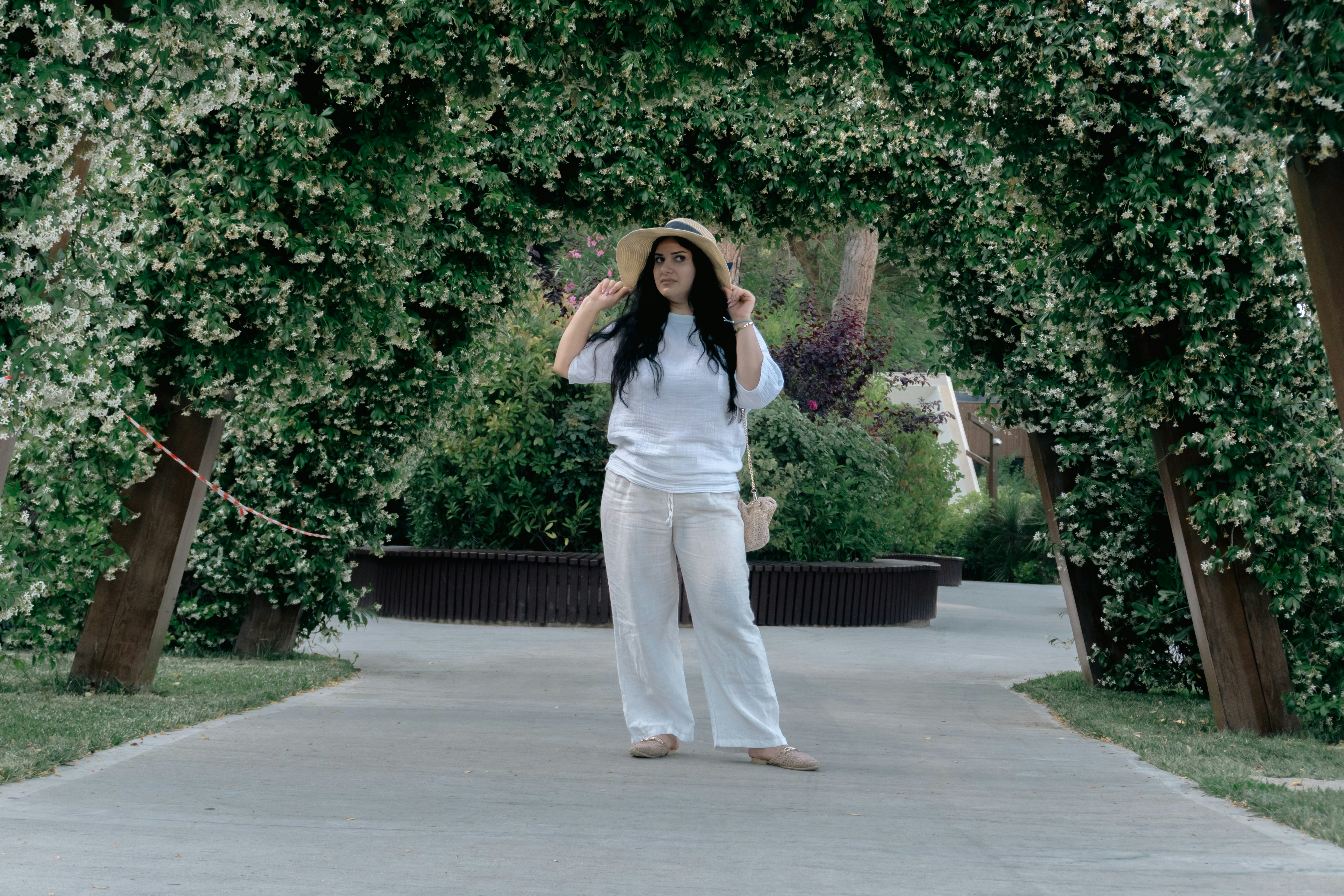 Young woman in white clothing and hat under blooming archway.