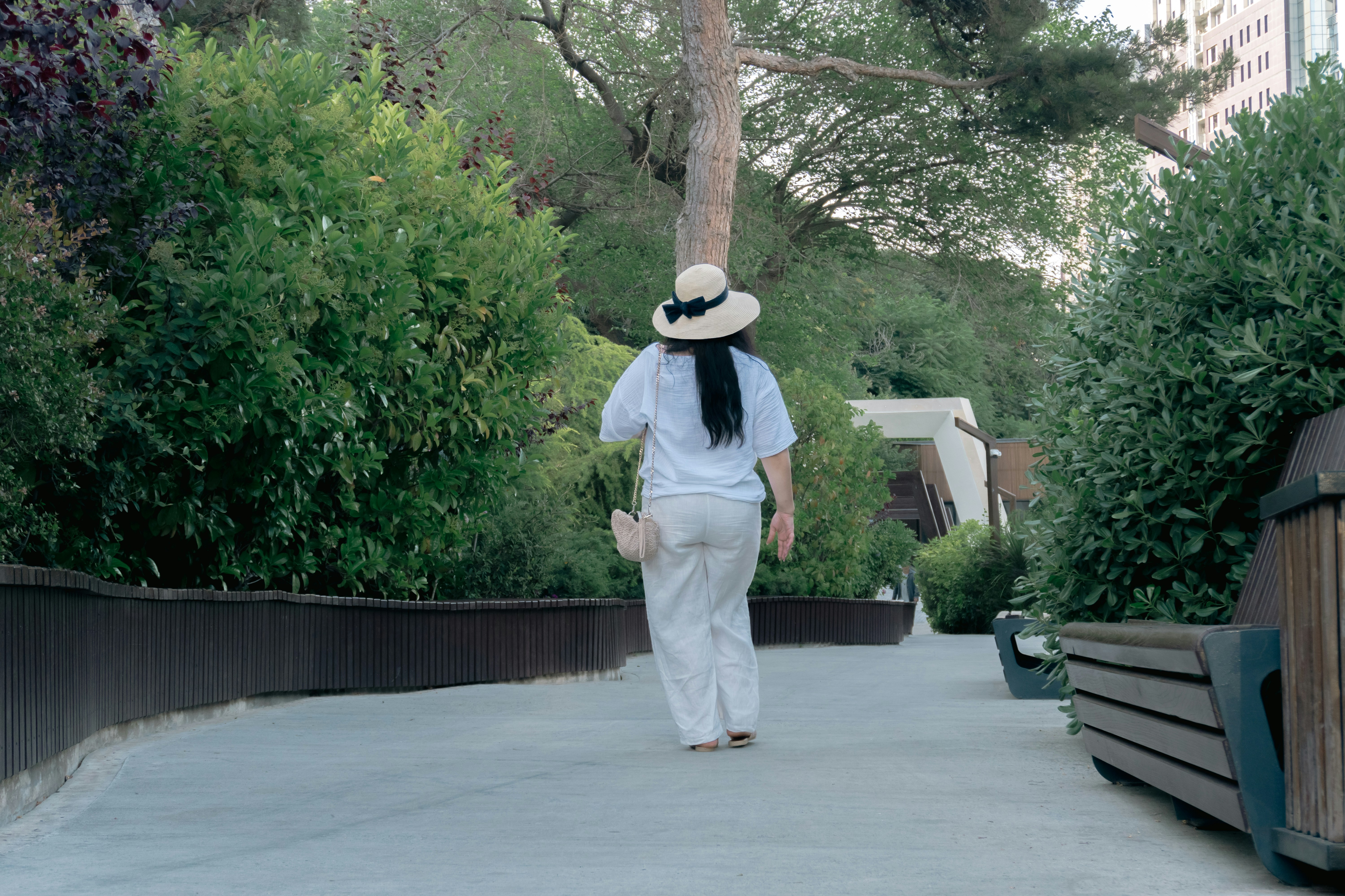 A woman walks on a path surrounded by green foliage.