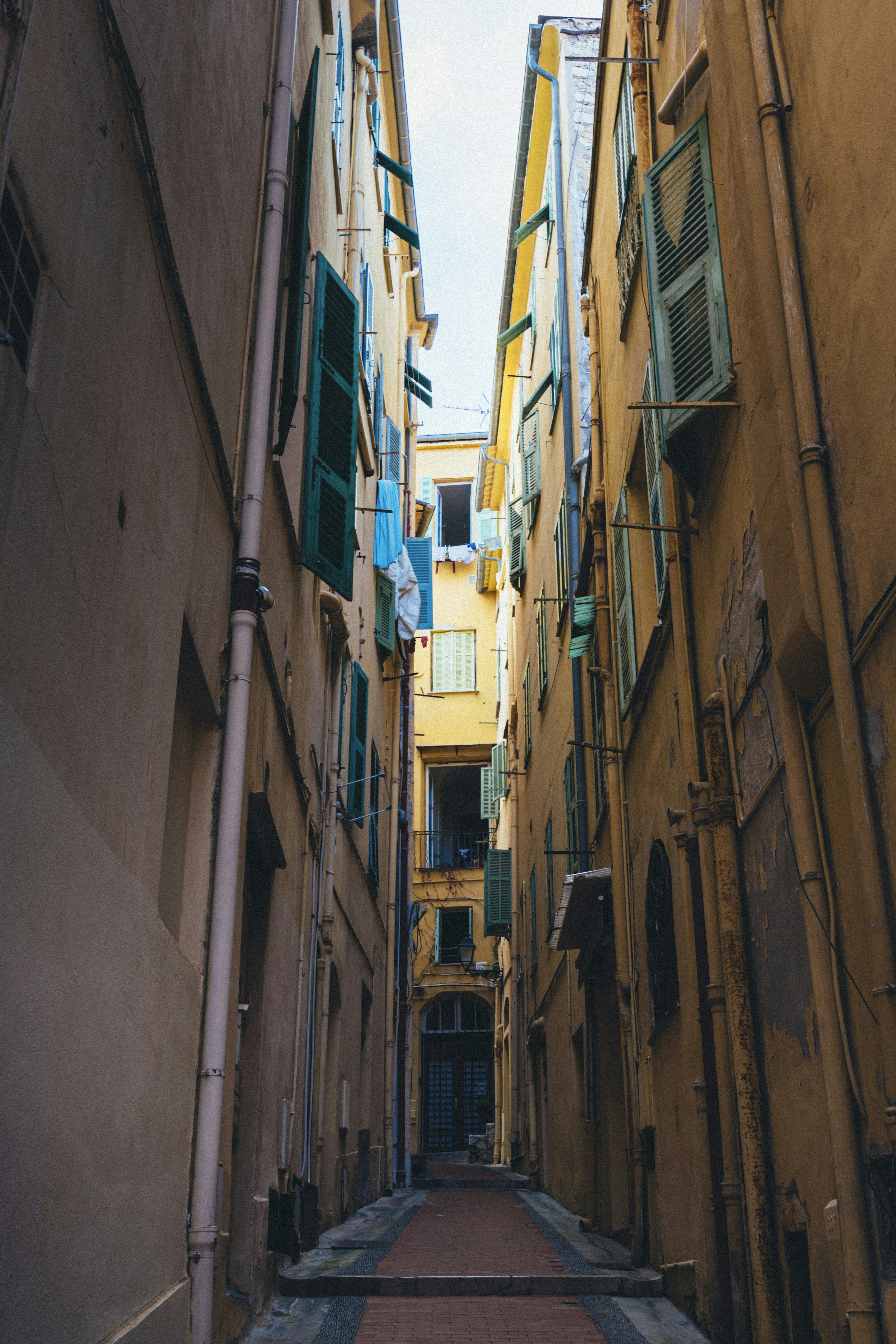 Narrow european alleyway between old buildings with green shutters.