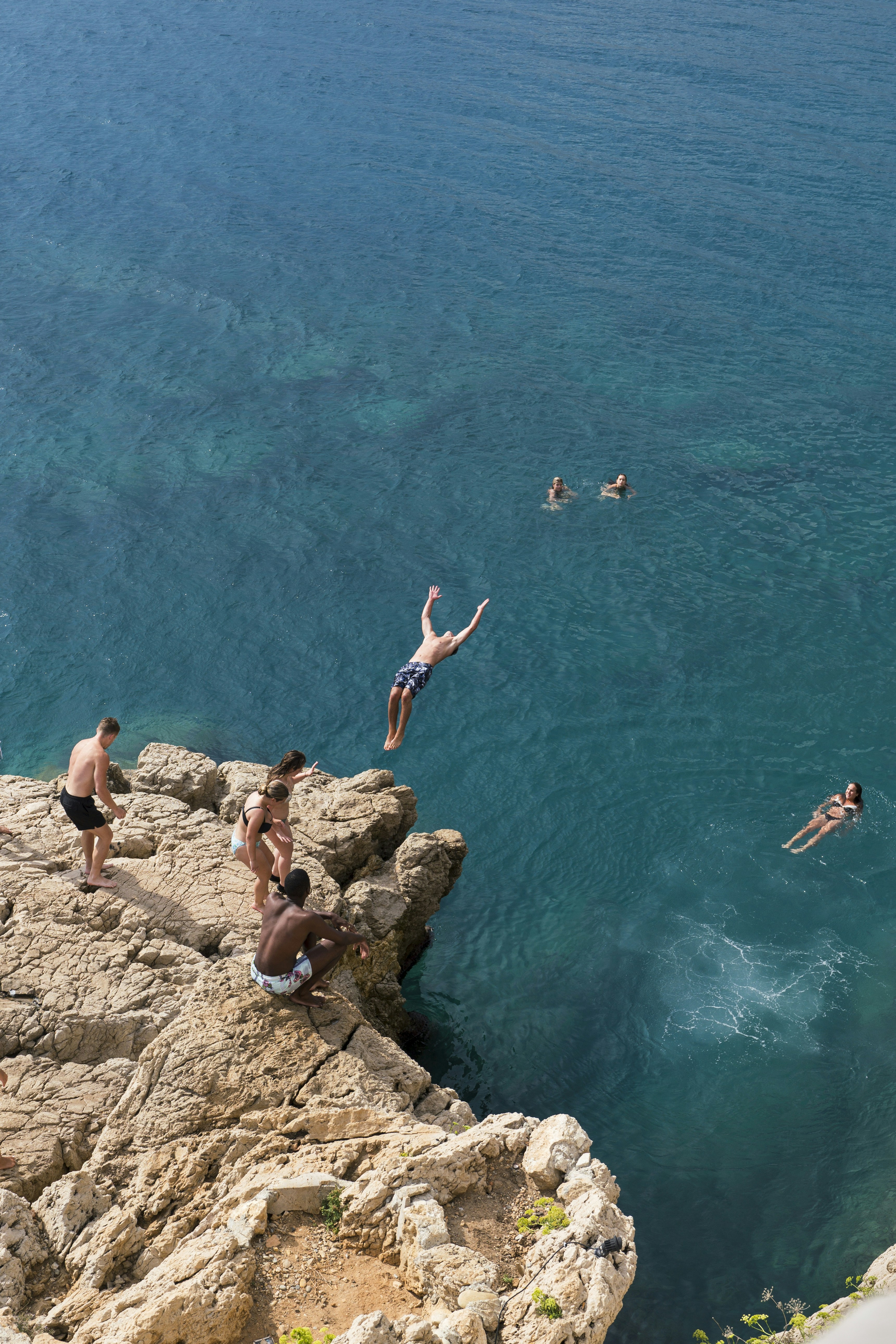 A man dives from a cliff into the turquoise sea.