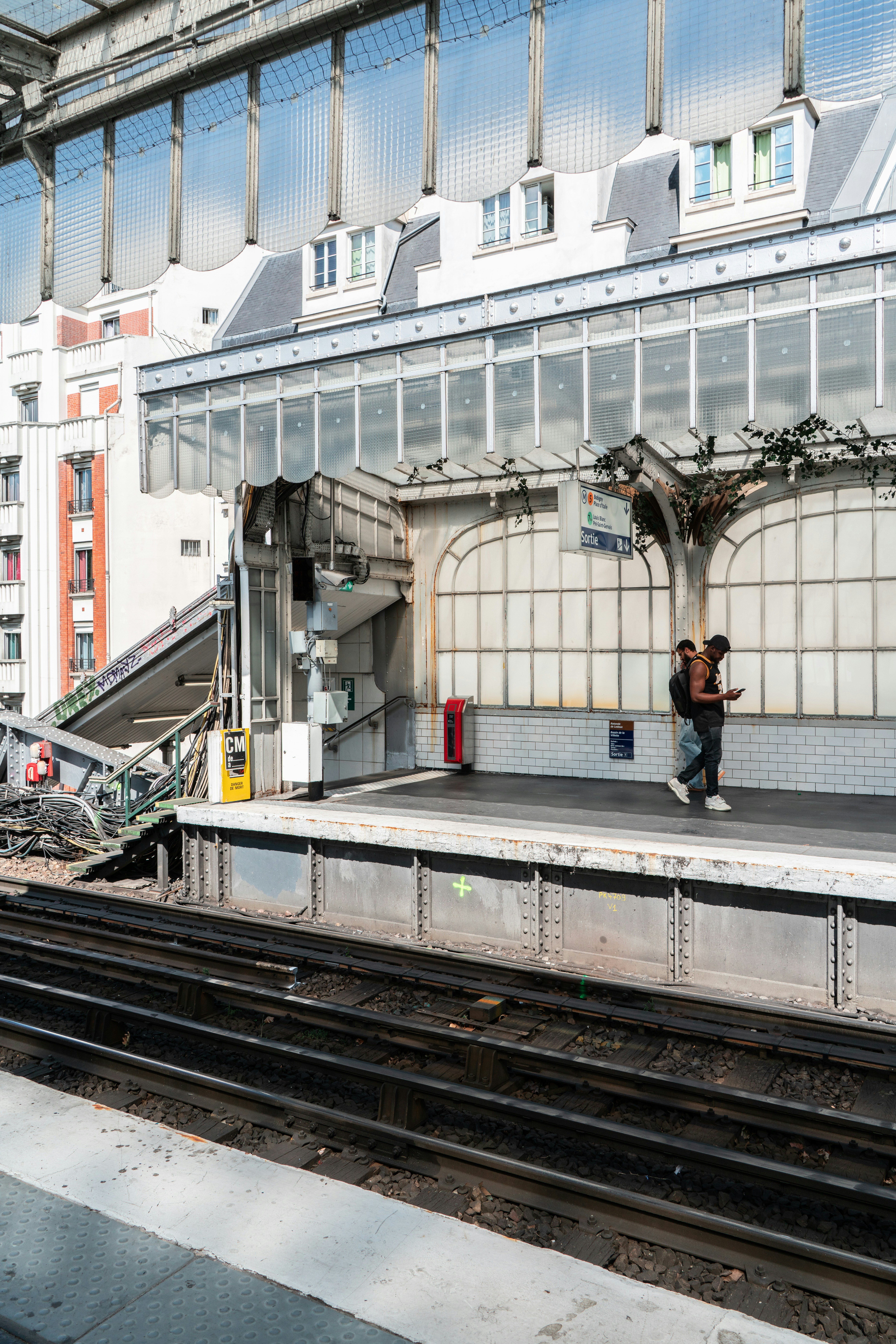 Due persone attendono su una banchina della stazione ferroviaria con binari.