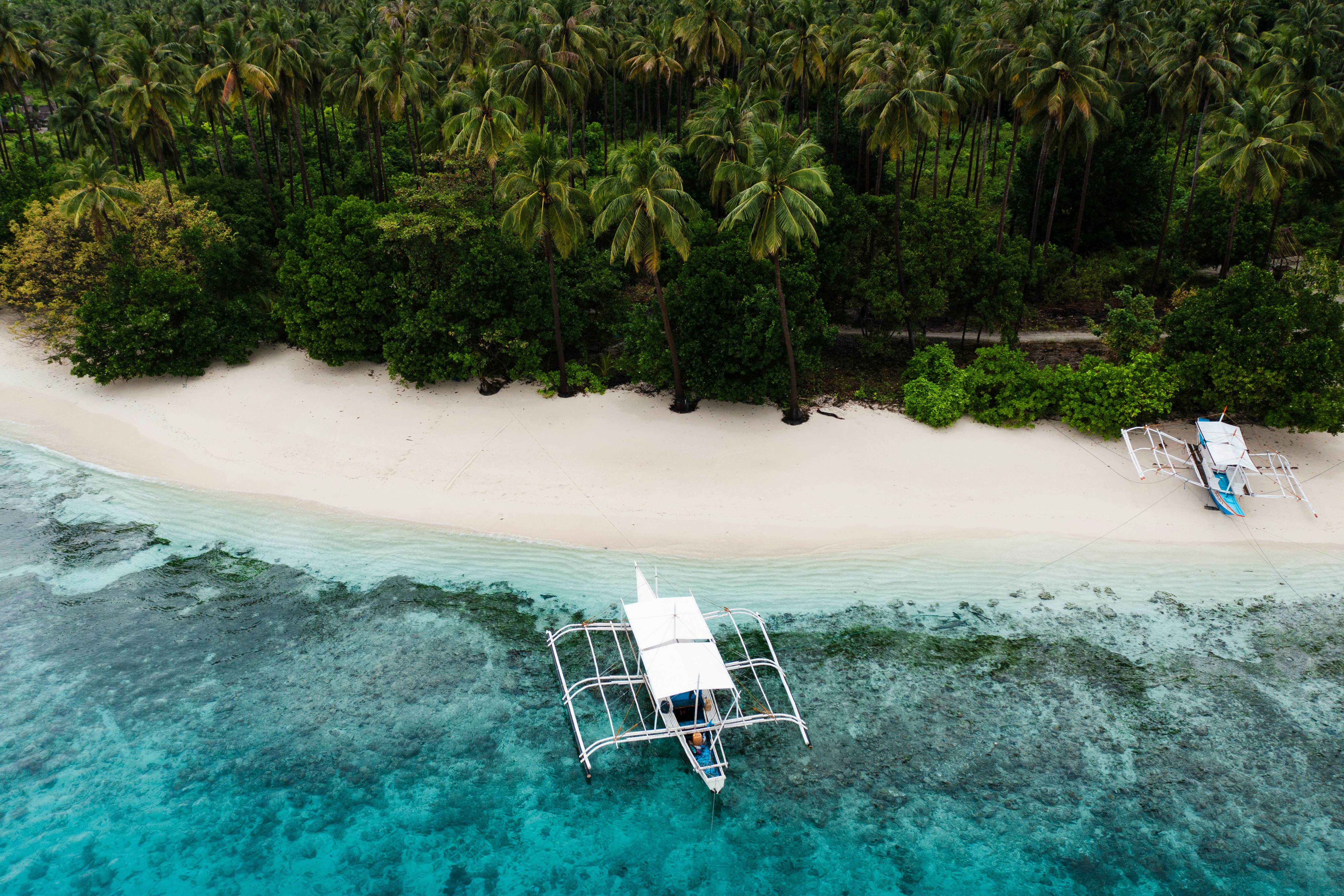 Tropical beach with white sand, turquoise water, and outrigger boat.