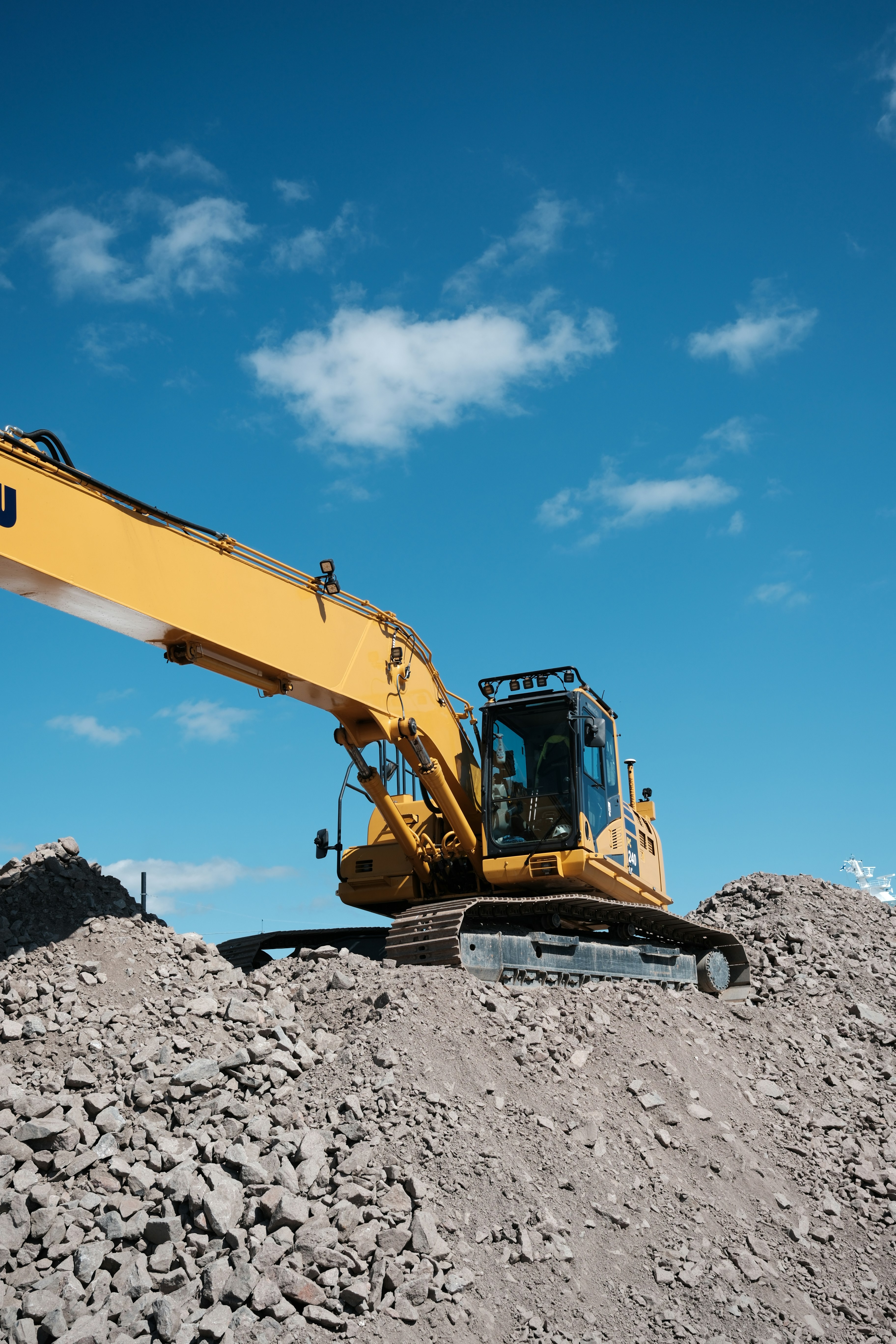 Yellow excavator on dirt piles beneath a blue sky