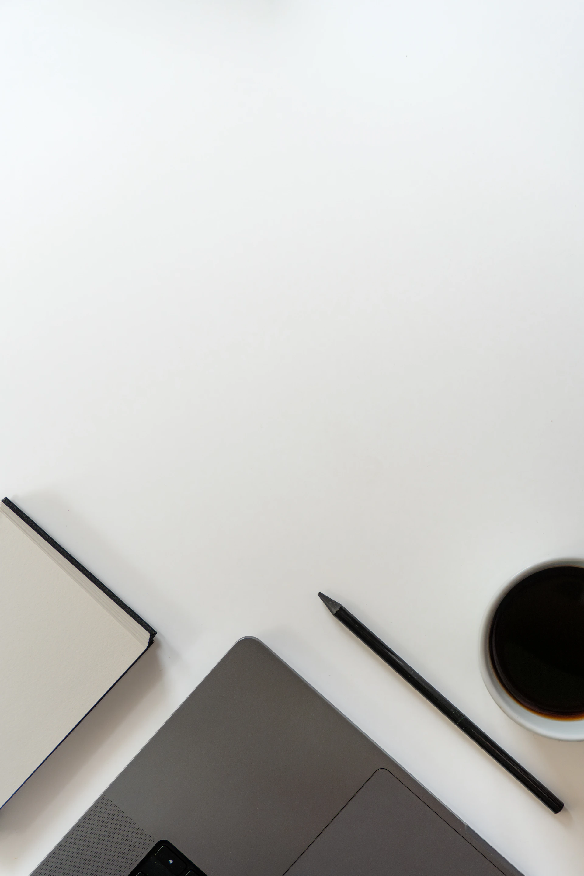 Laptop, notebook, pencil, and coffee cup on a white desk.