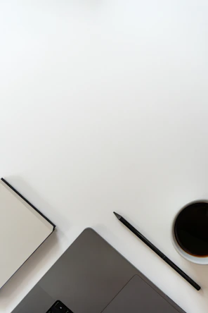 Laptop, notebook, pencil, and coffee cup on a white desk