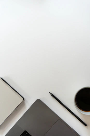 Laptop, notebook, pencil, and coffee cup on a white desk