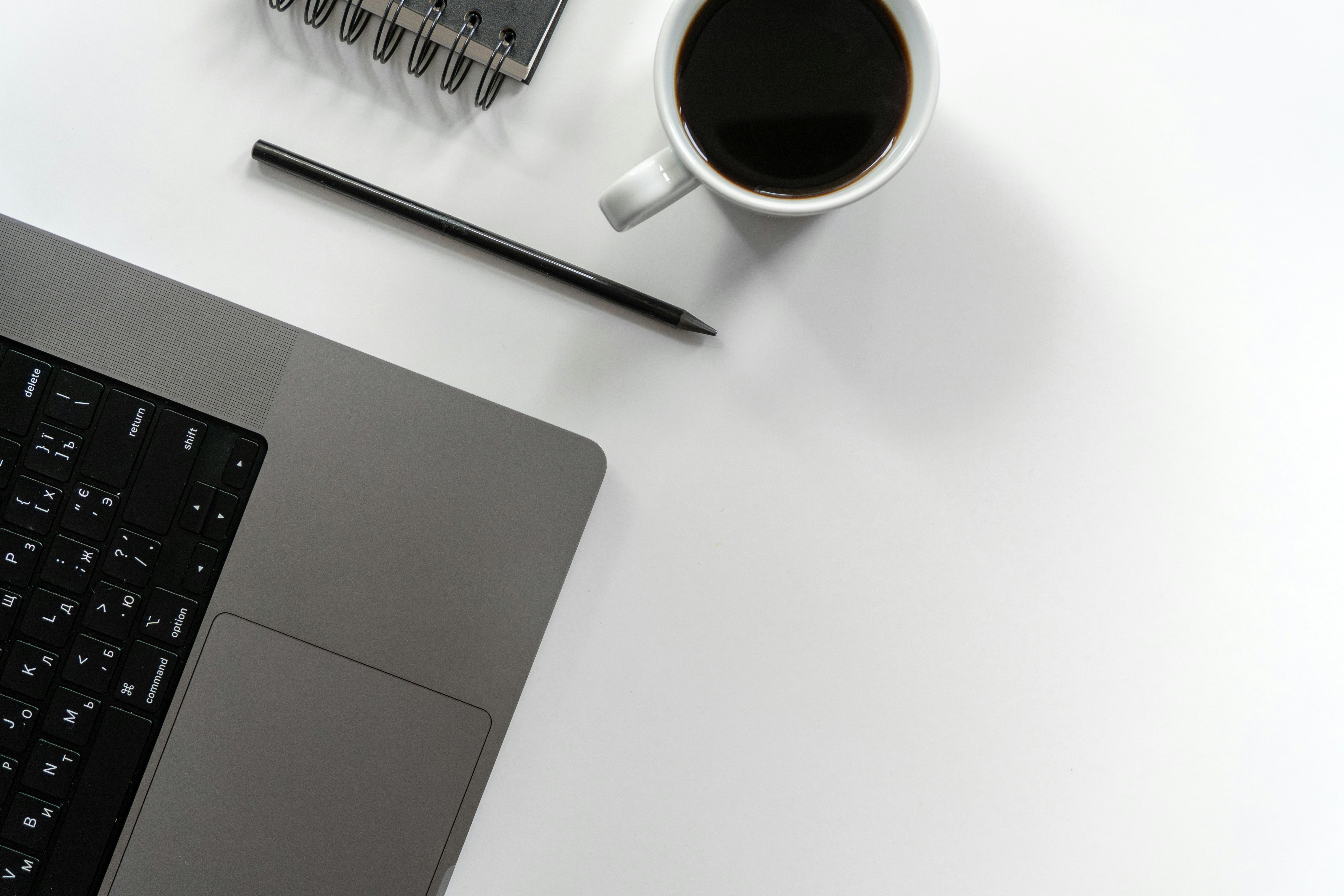 Laptop, coffee, pen, and notebook on a white desk.