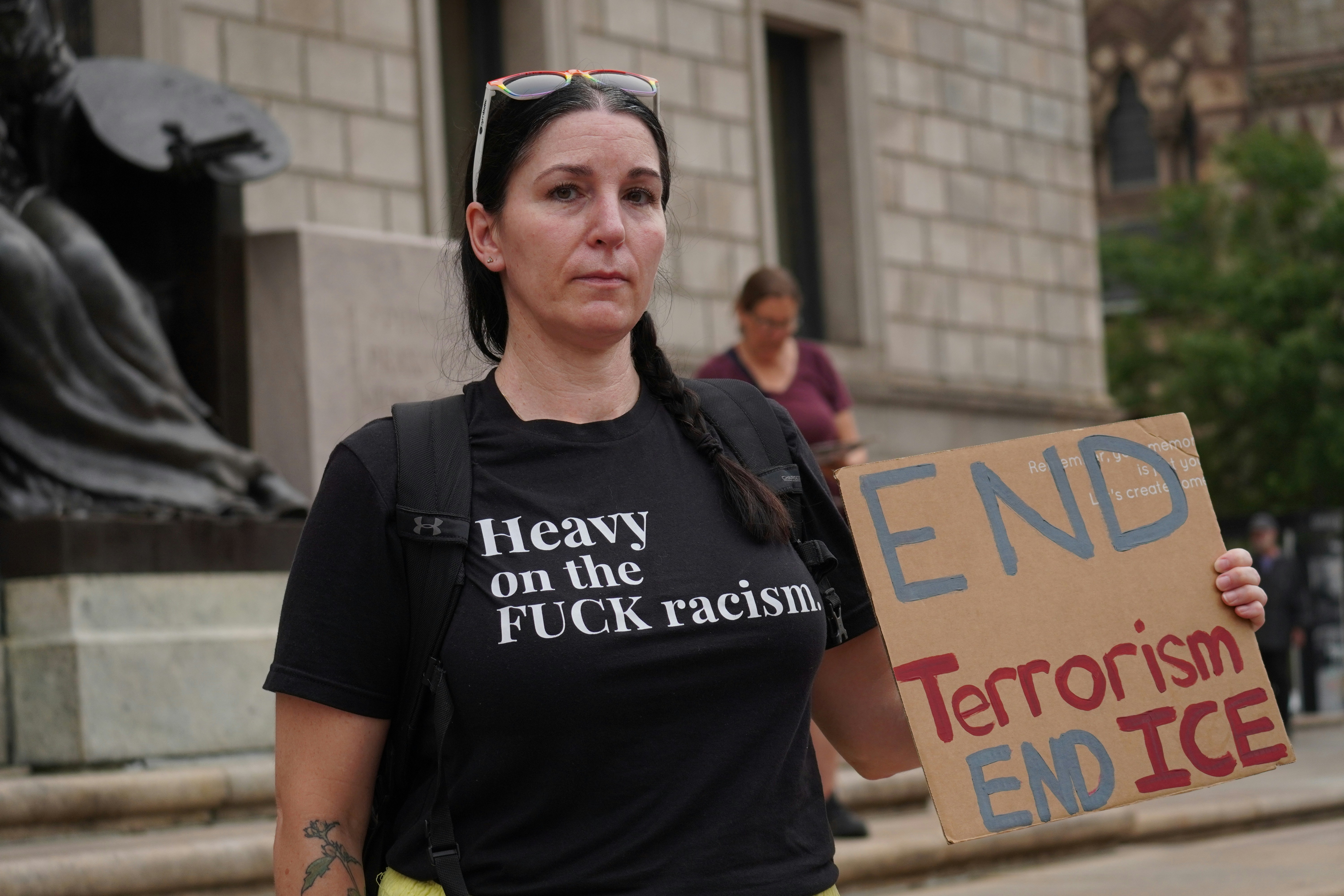 Woman in anti-racism shirt holding "end ice" protest sign.