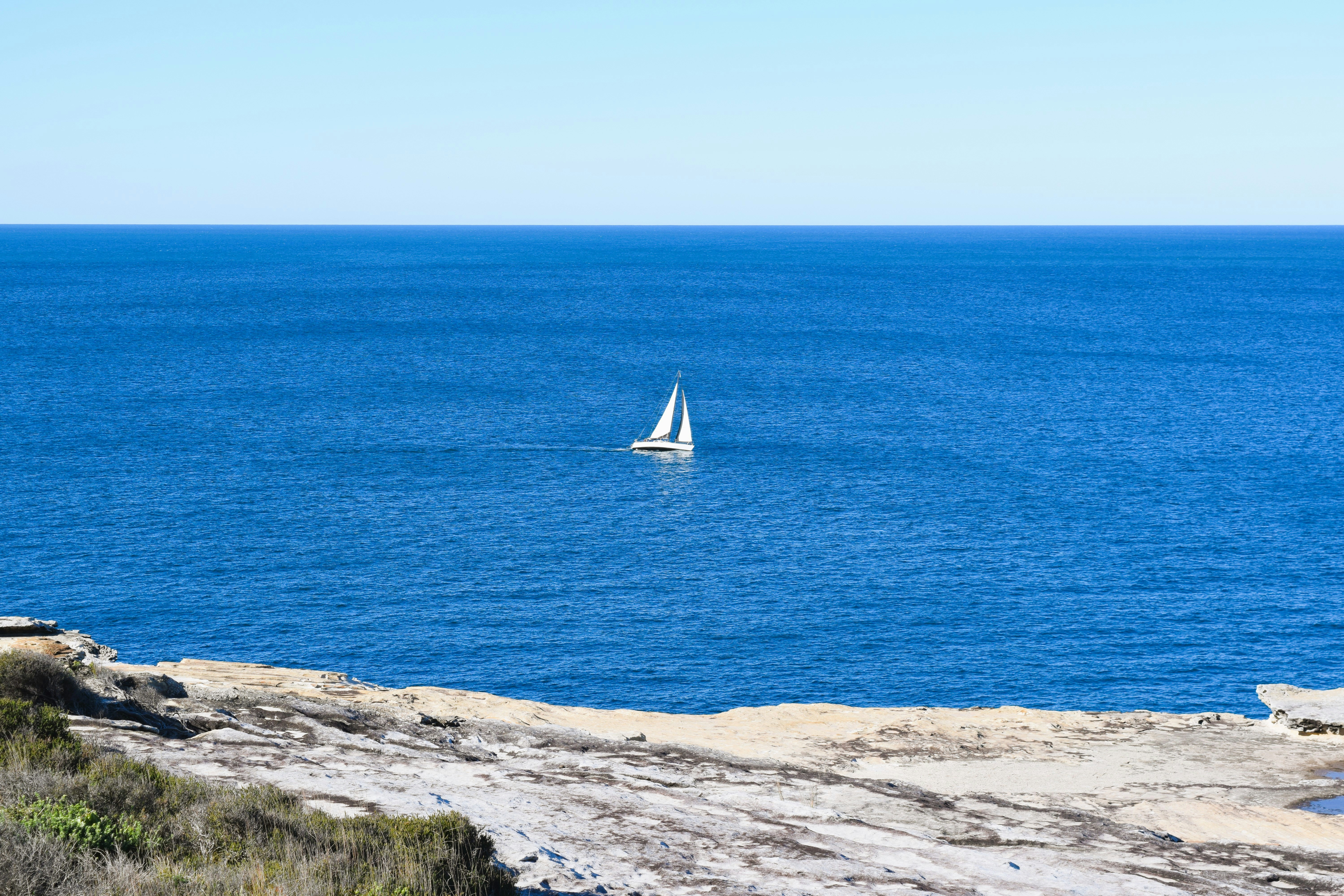 Ein Segelboot auf einem blauen Ozean nahe einer felsigen Küste.