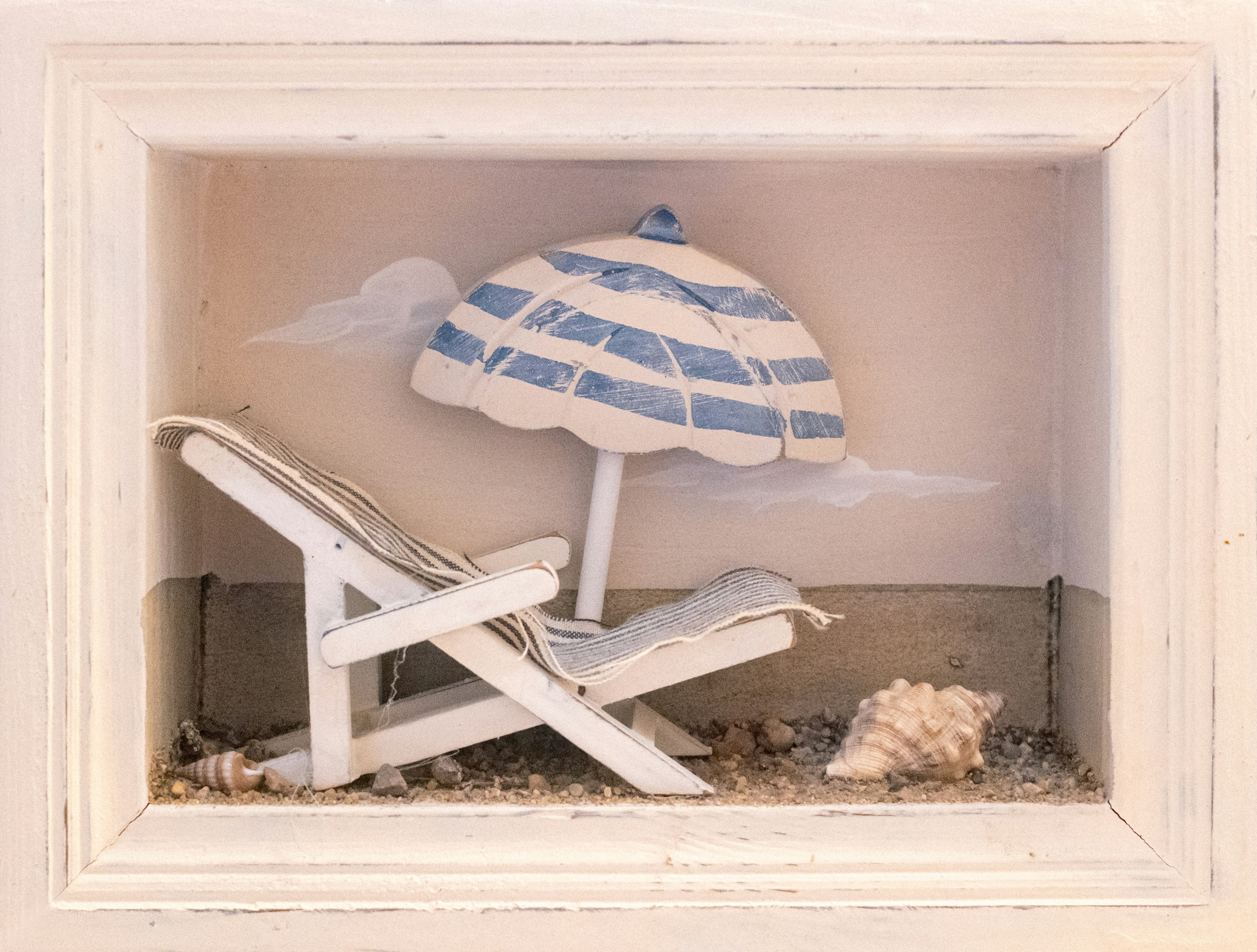Miniature beach scene with white chair, striped umbrella, and seashell.