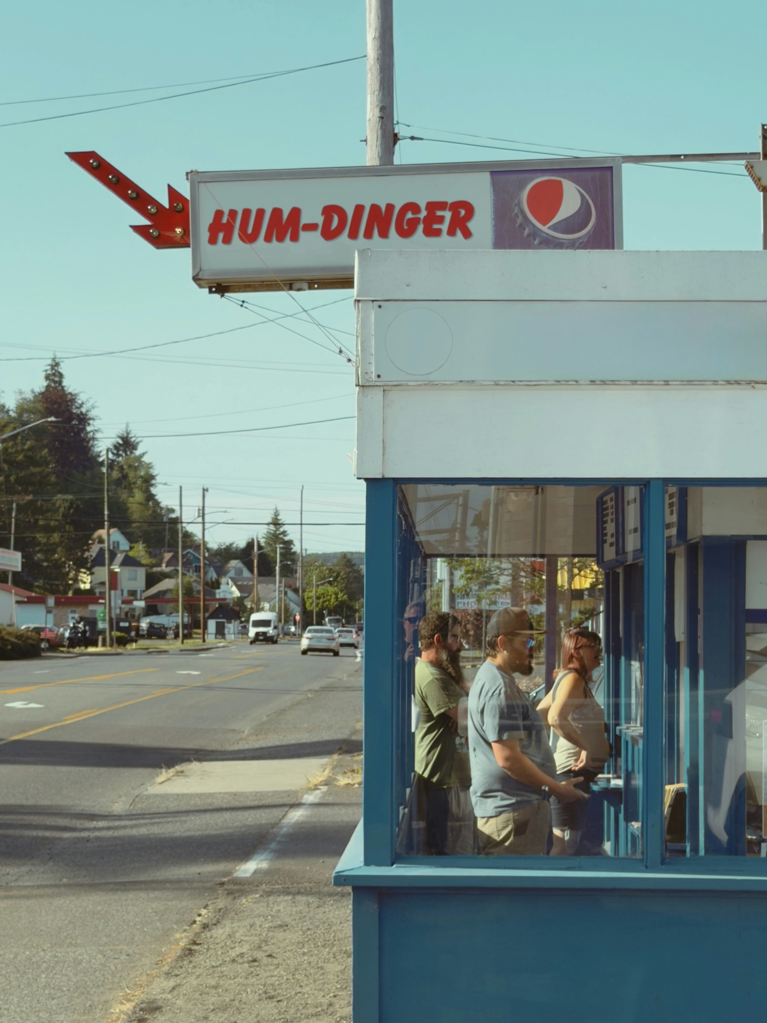 People inside a hum-dinger stand next to a street.