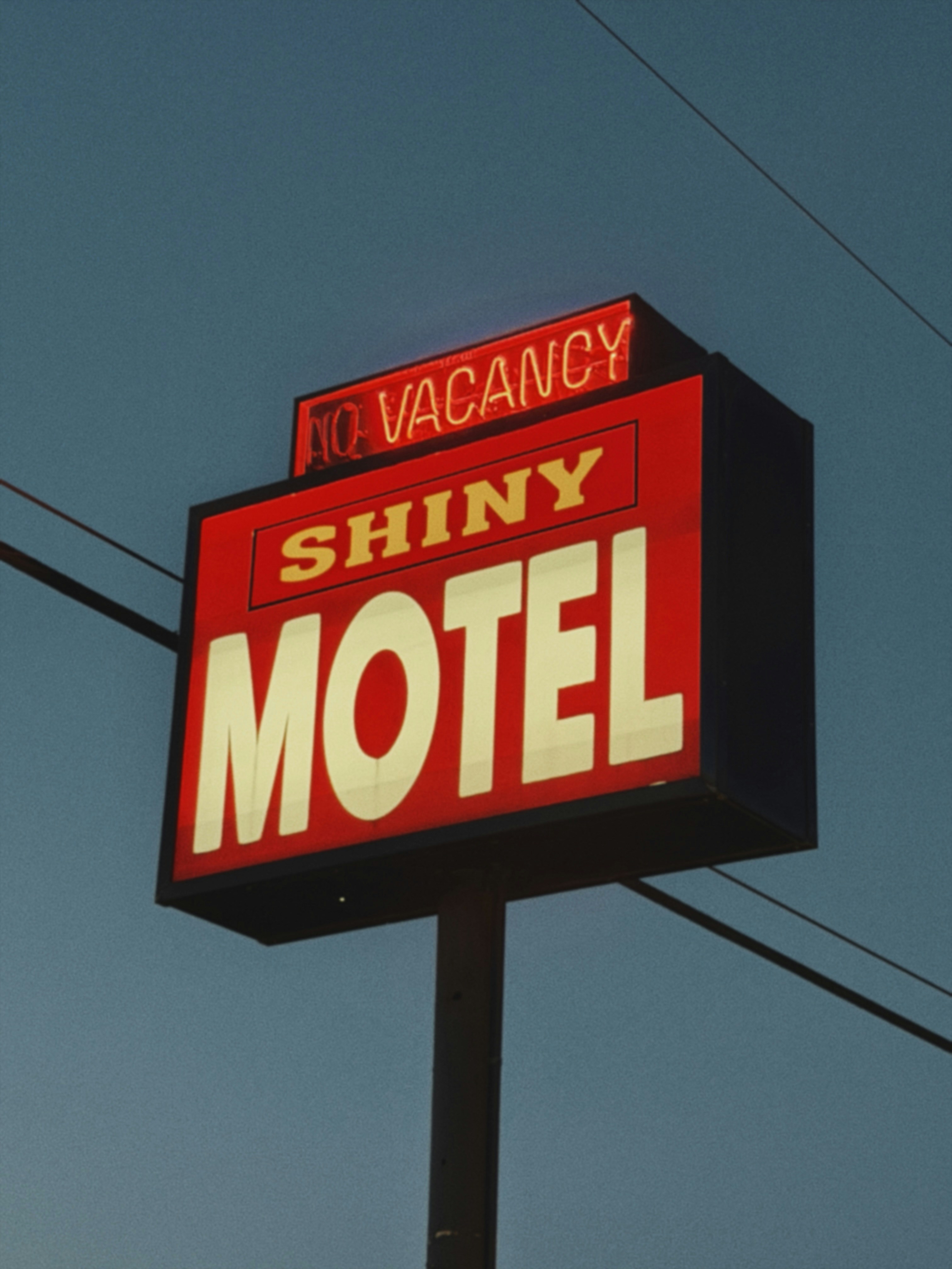 A red neon "shiny motel" sign with "no vacancy" illuminated.