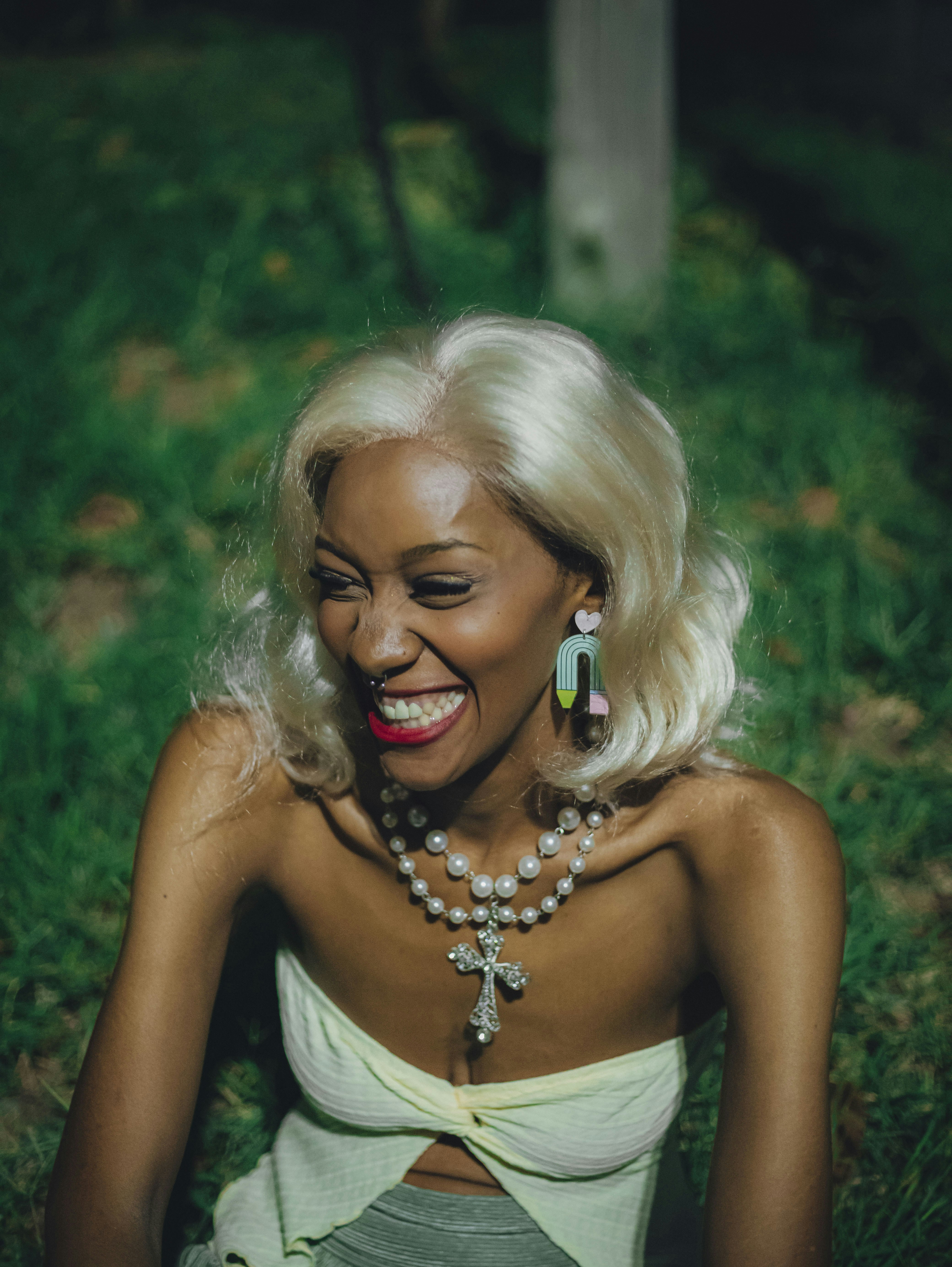 Mujer feliz con pelo rubio y joyas riendo al aire libre.
