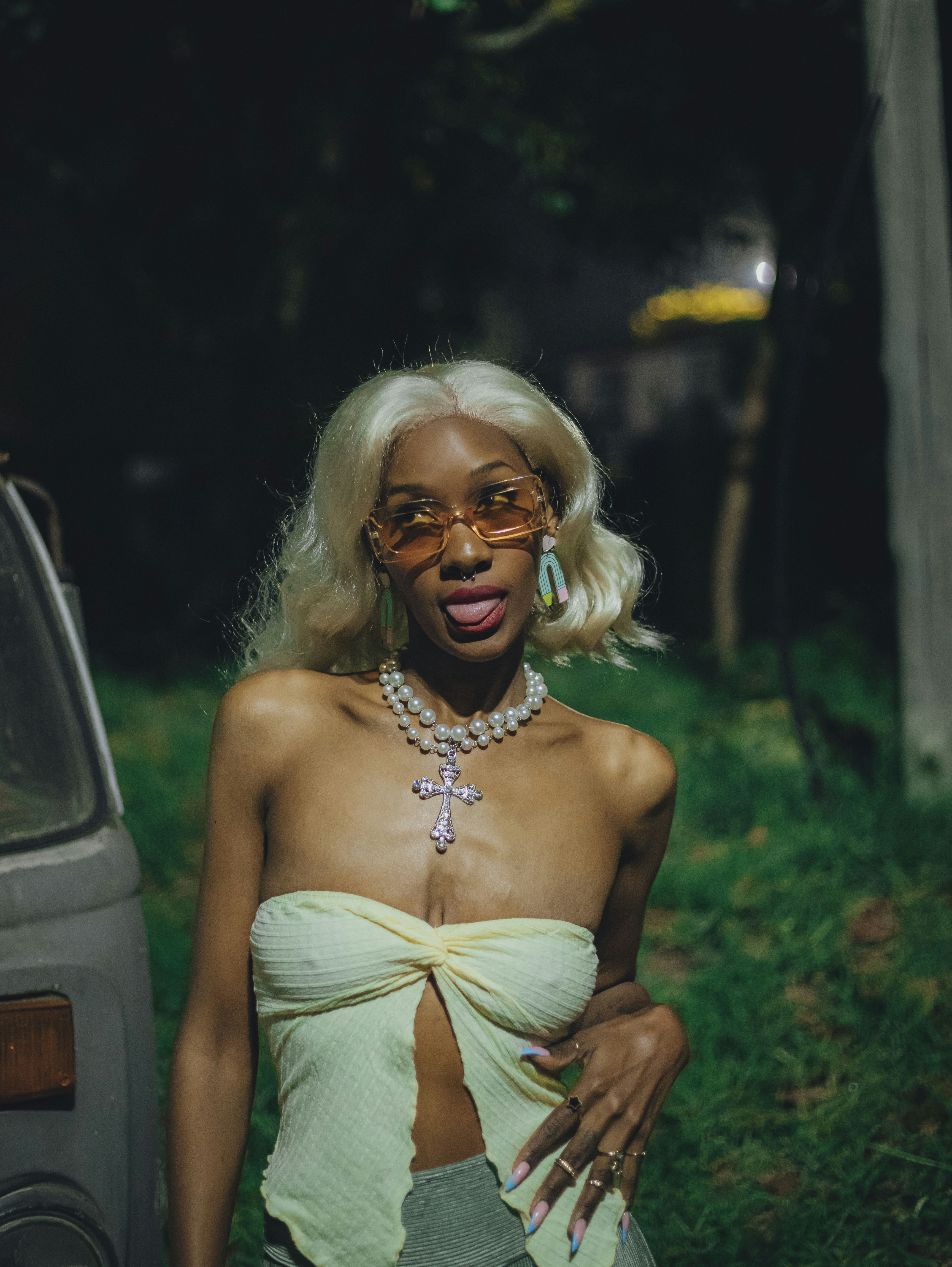 Mujer rubia con gafas de sol y perlas posa al aire libre por la noche.