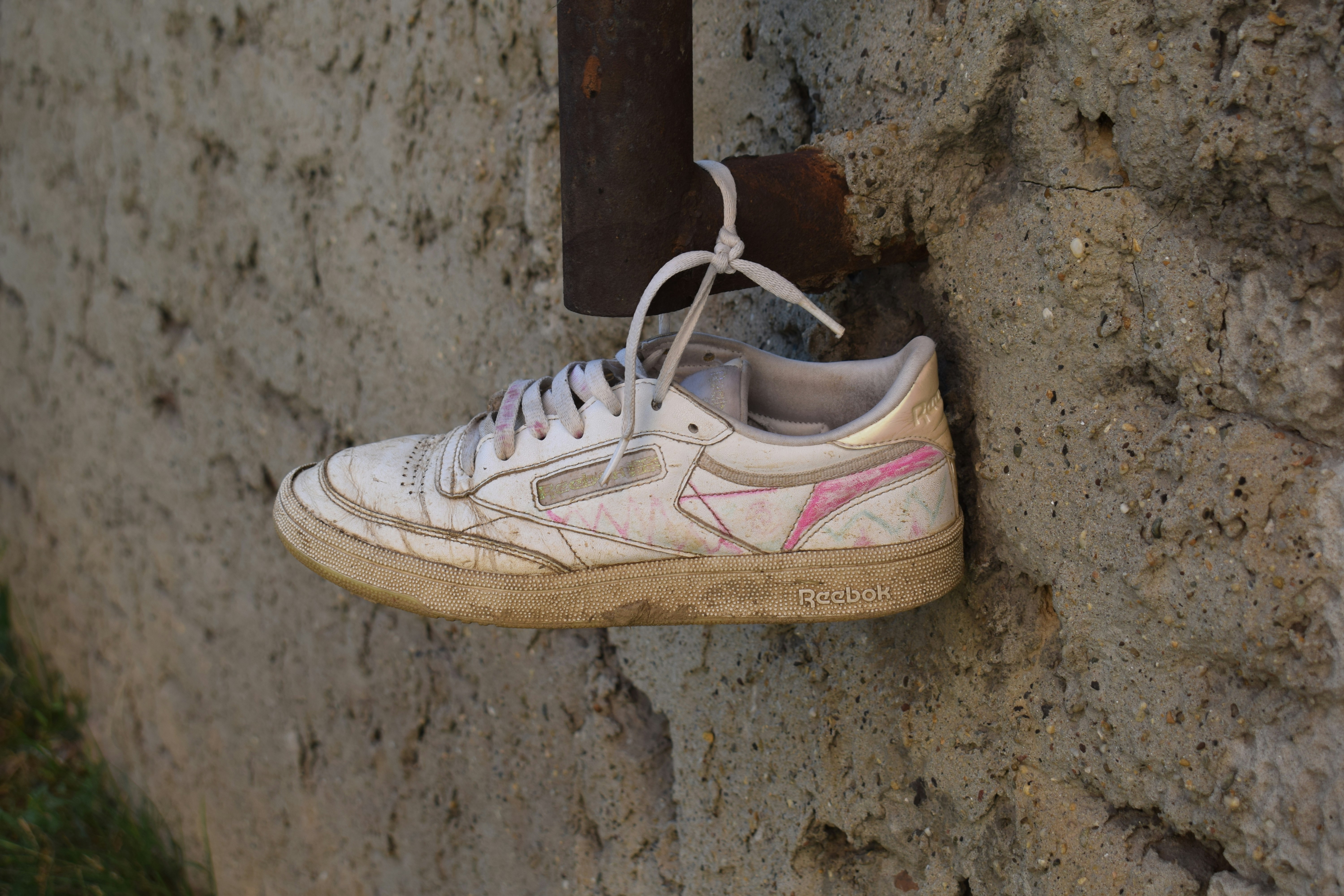 An old, dirty white sneaker hangs from a rusty pipe.